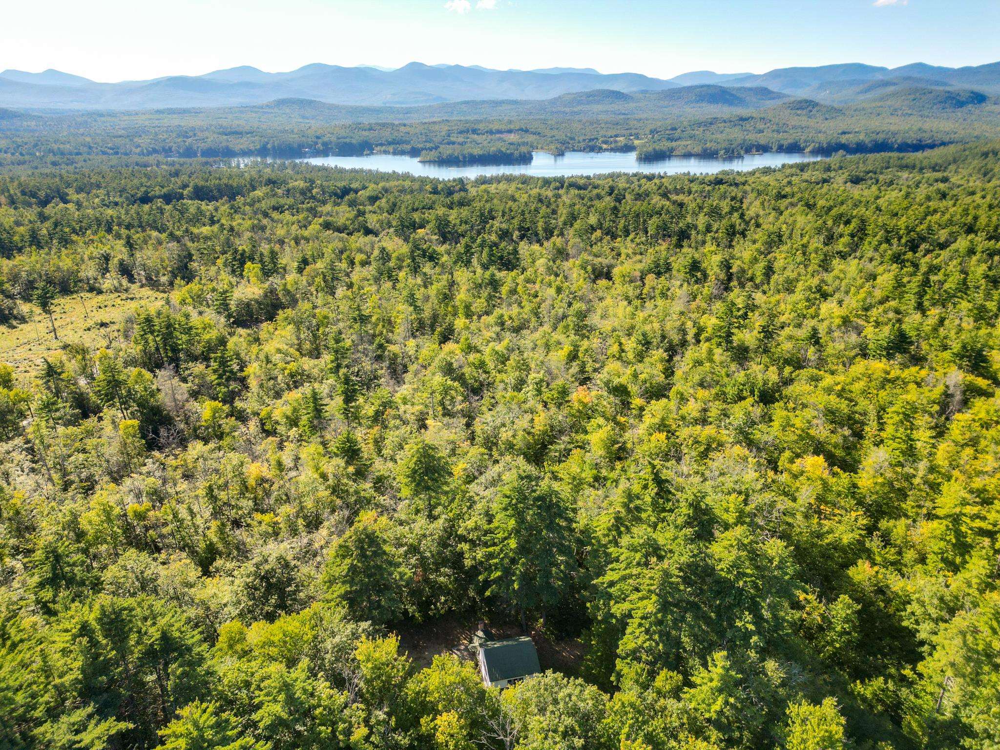 Small cabin amid forest, with a lake and distant mountain ridges.