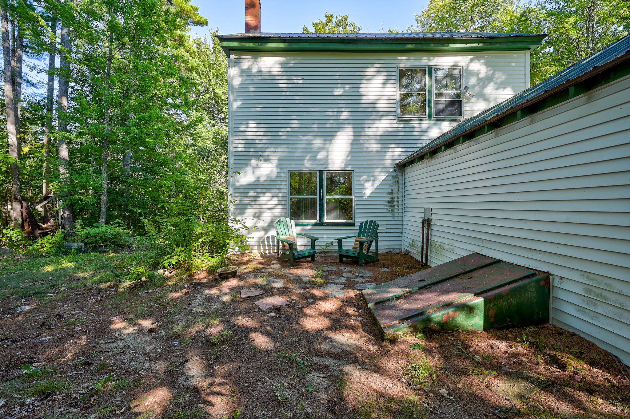 House rear patio with two green Adirondack chairs beside a wooded yard.