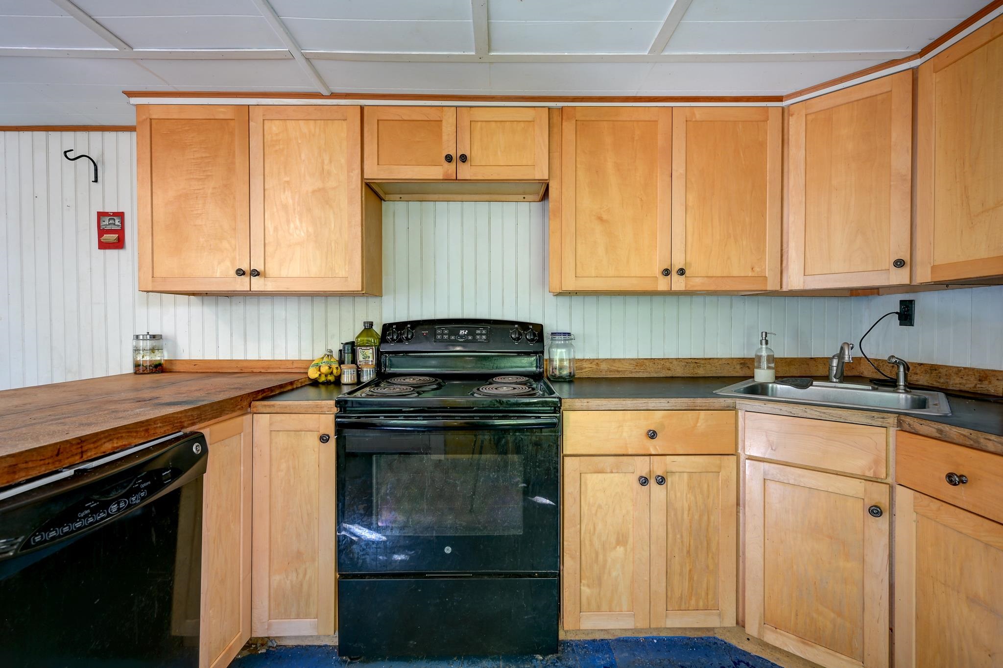 Kitchen with light wood cabinetry, butcher-block counter, black range, and stainless-steel sink.