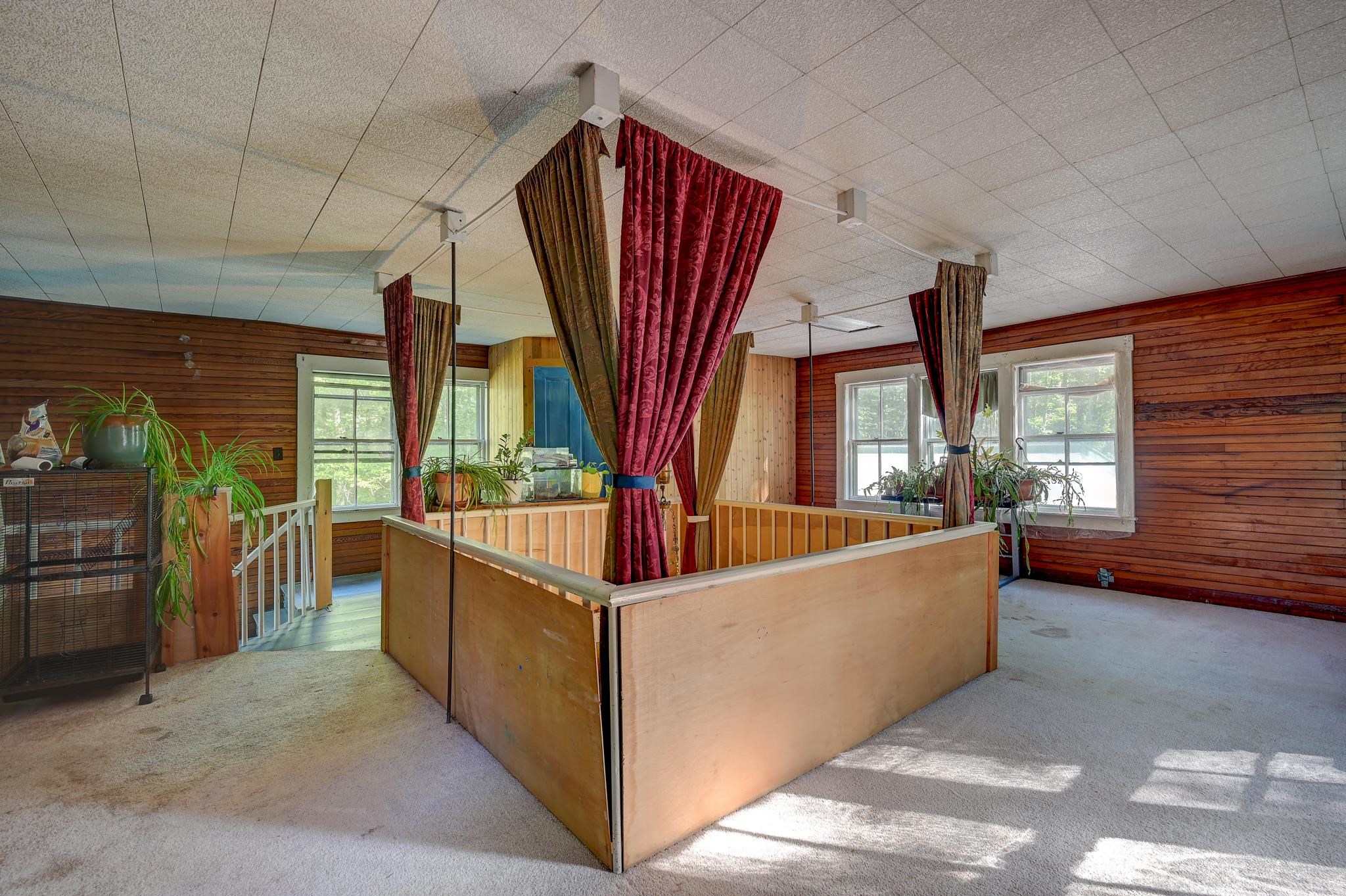 Carpeted room with wood-paneled walls and a curtained wooden enclosure beneath several windows.