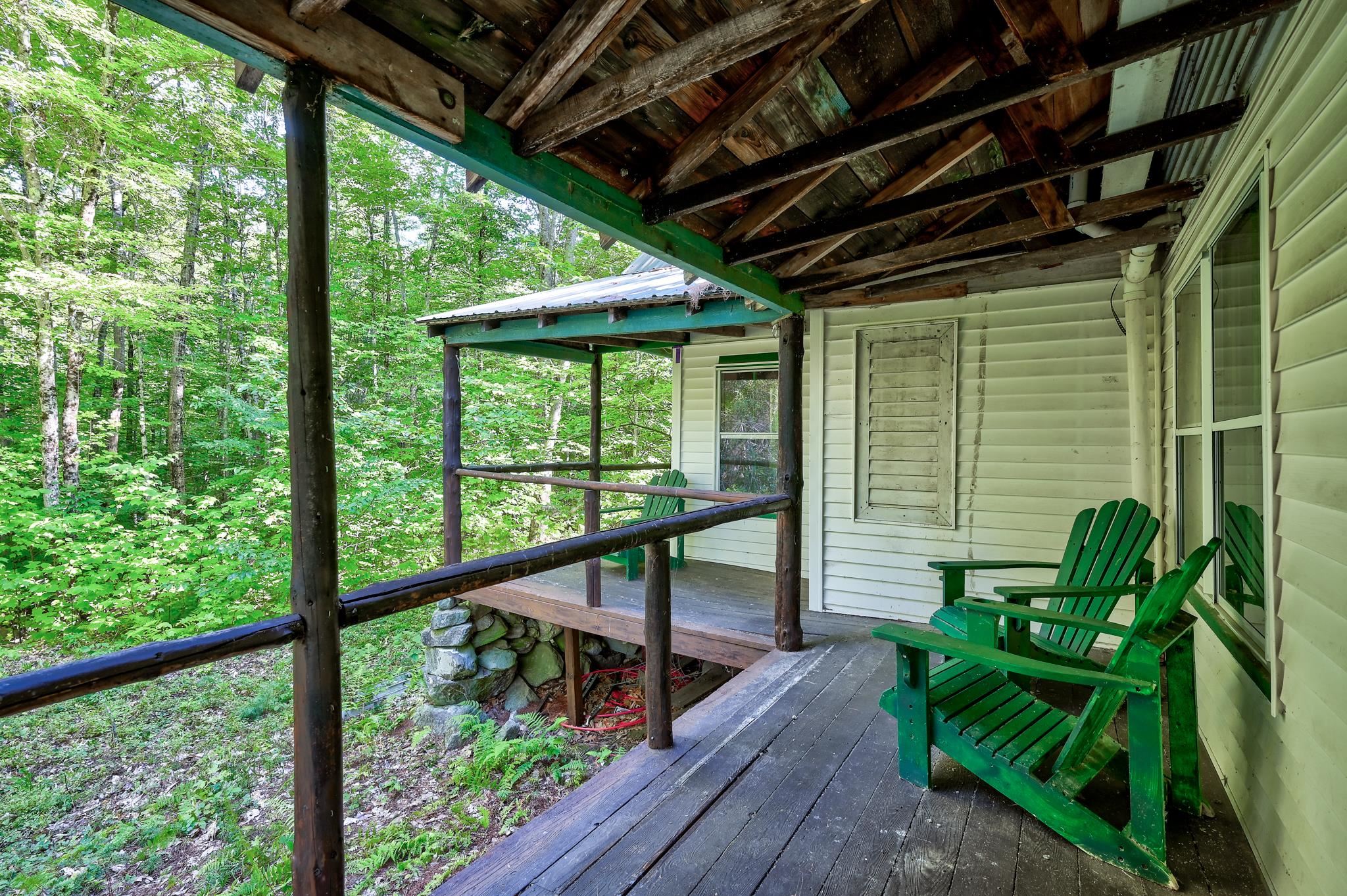 Covered woodland porch with exposed beams and green Adirondack chairs.
