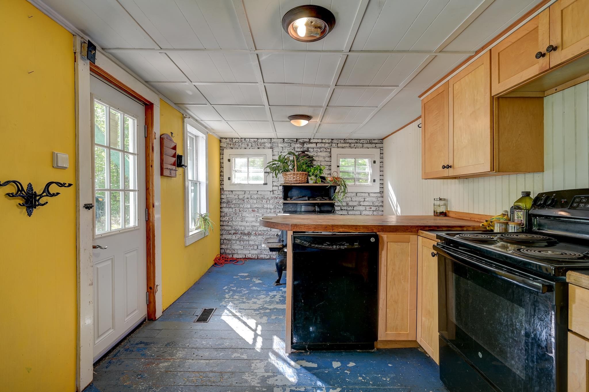 Kitchen with yellow walls, wood cabinets, a brick accent wall, and a worn blue plank floor.
