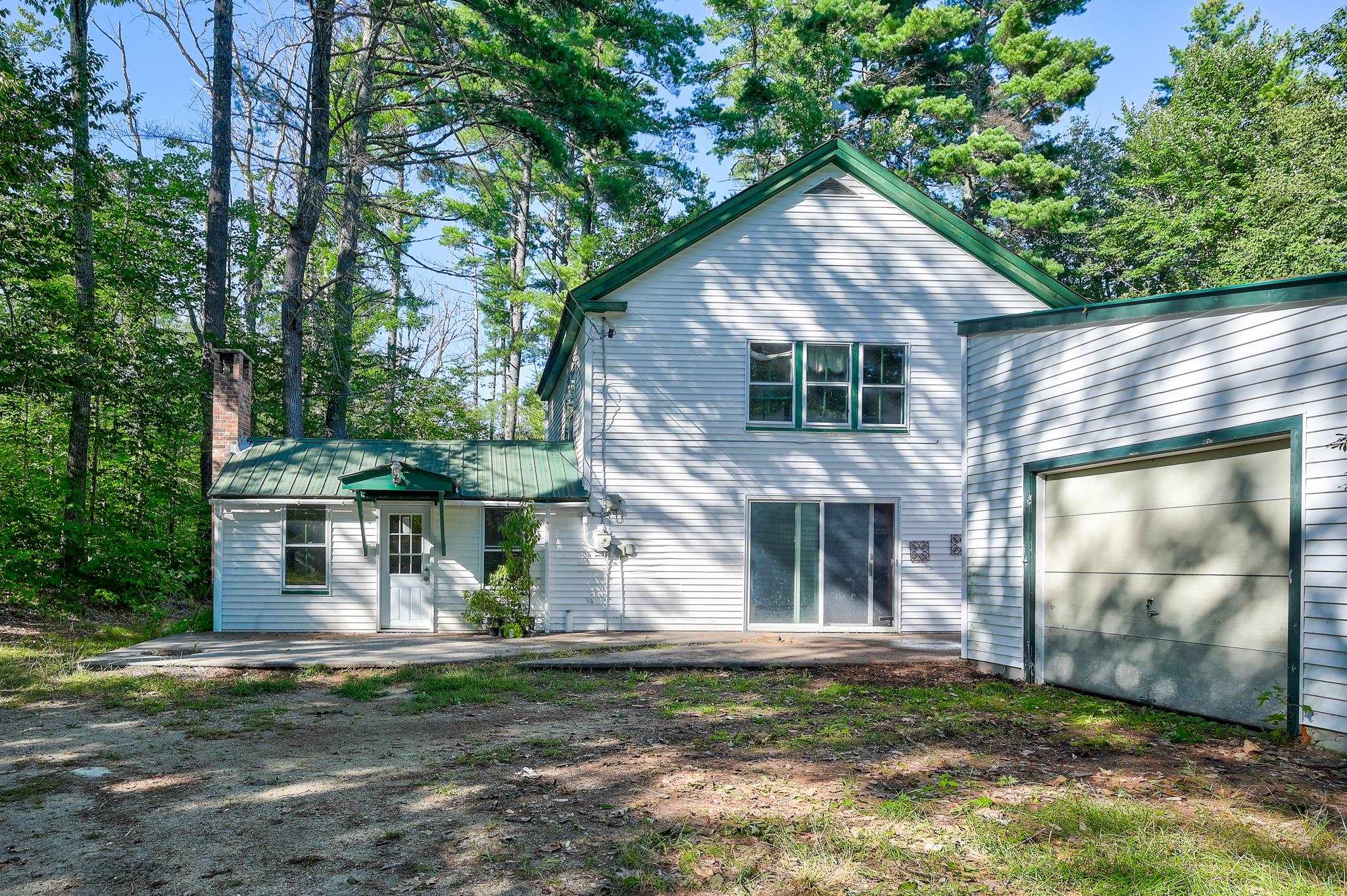White two-story house with green trim and attached garage among mature trees.