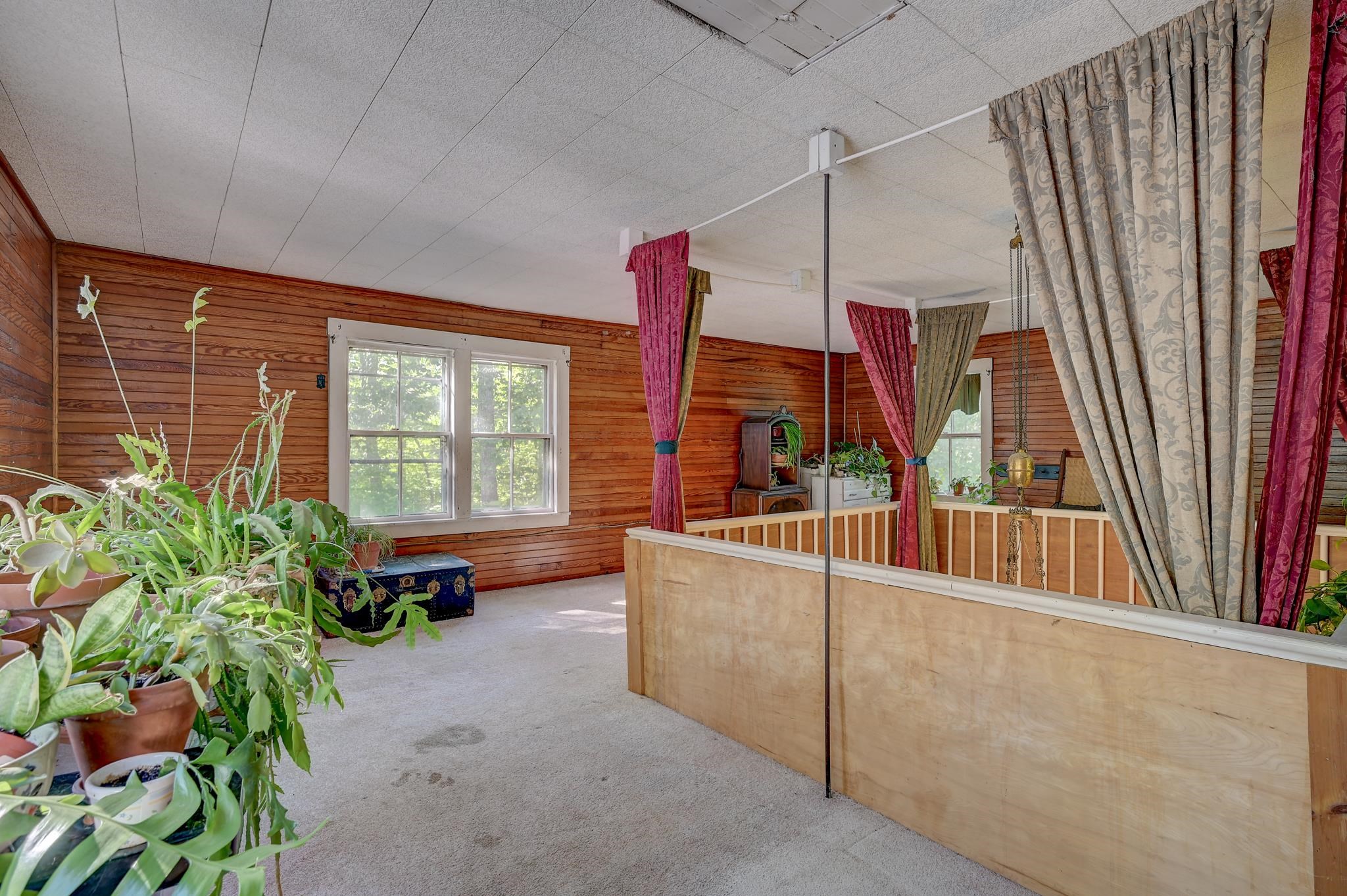 Upper-level room with wood-paneled walls, a low railing, and potted plants by the windows.