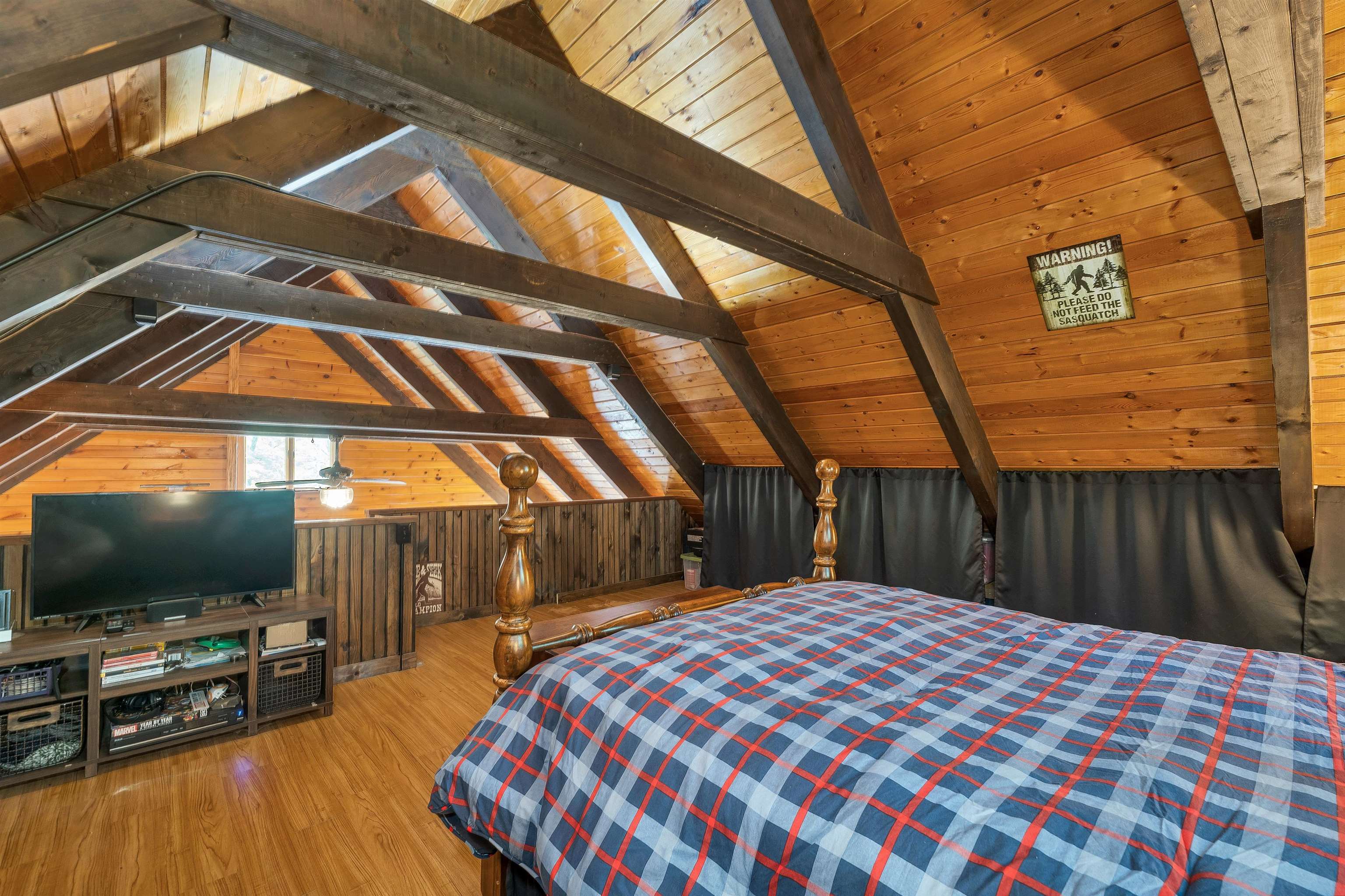 Attic bedroom with exposed timber beams, a plaid-covered bed, and a television.
