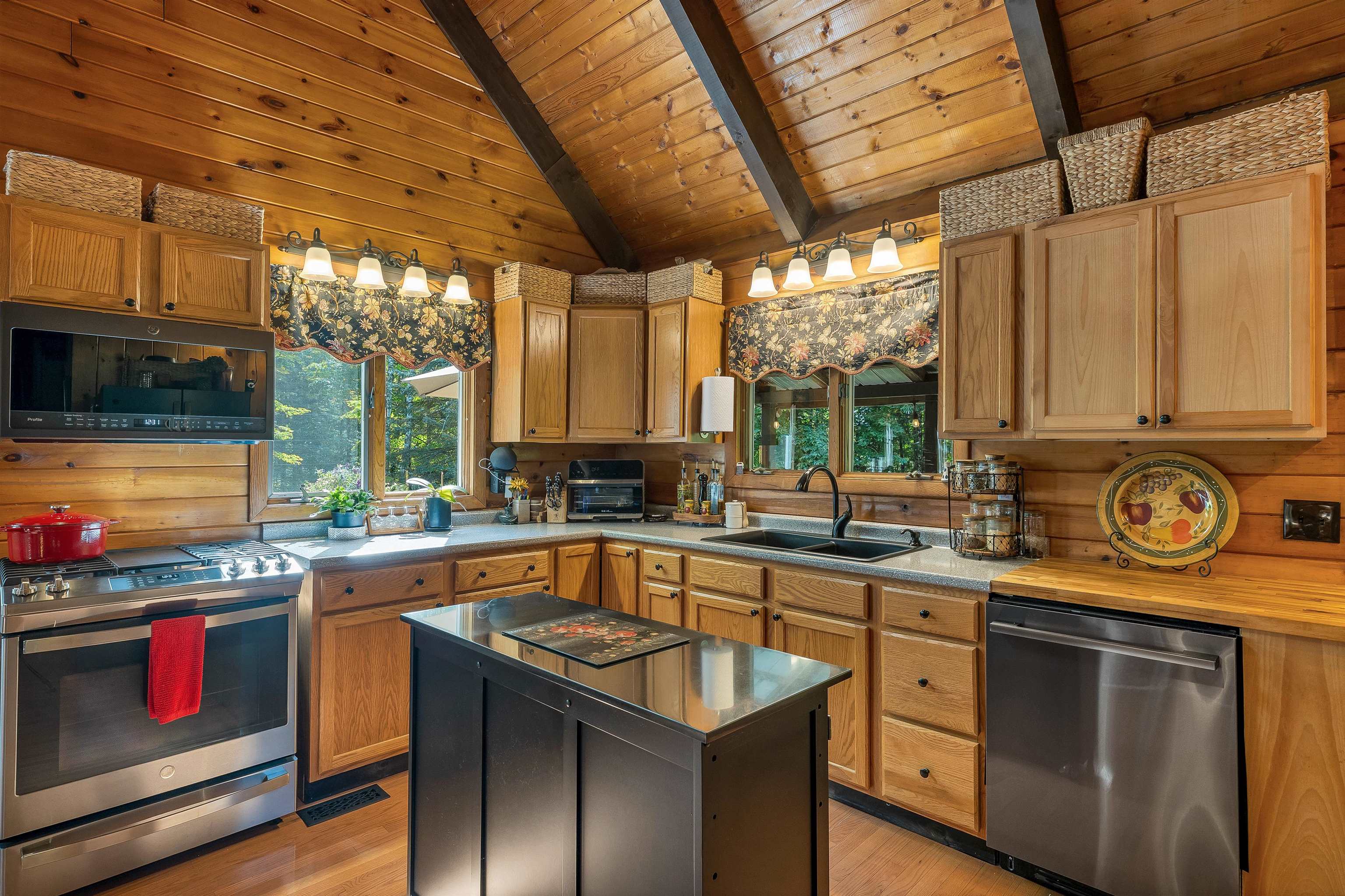 Rustic kitchen with wood cabinets, a vaulted beam ceiling, stainless steel appliances, and a glass-top island.