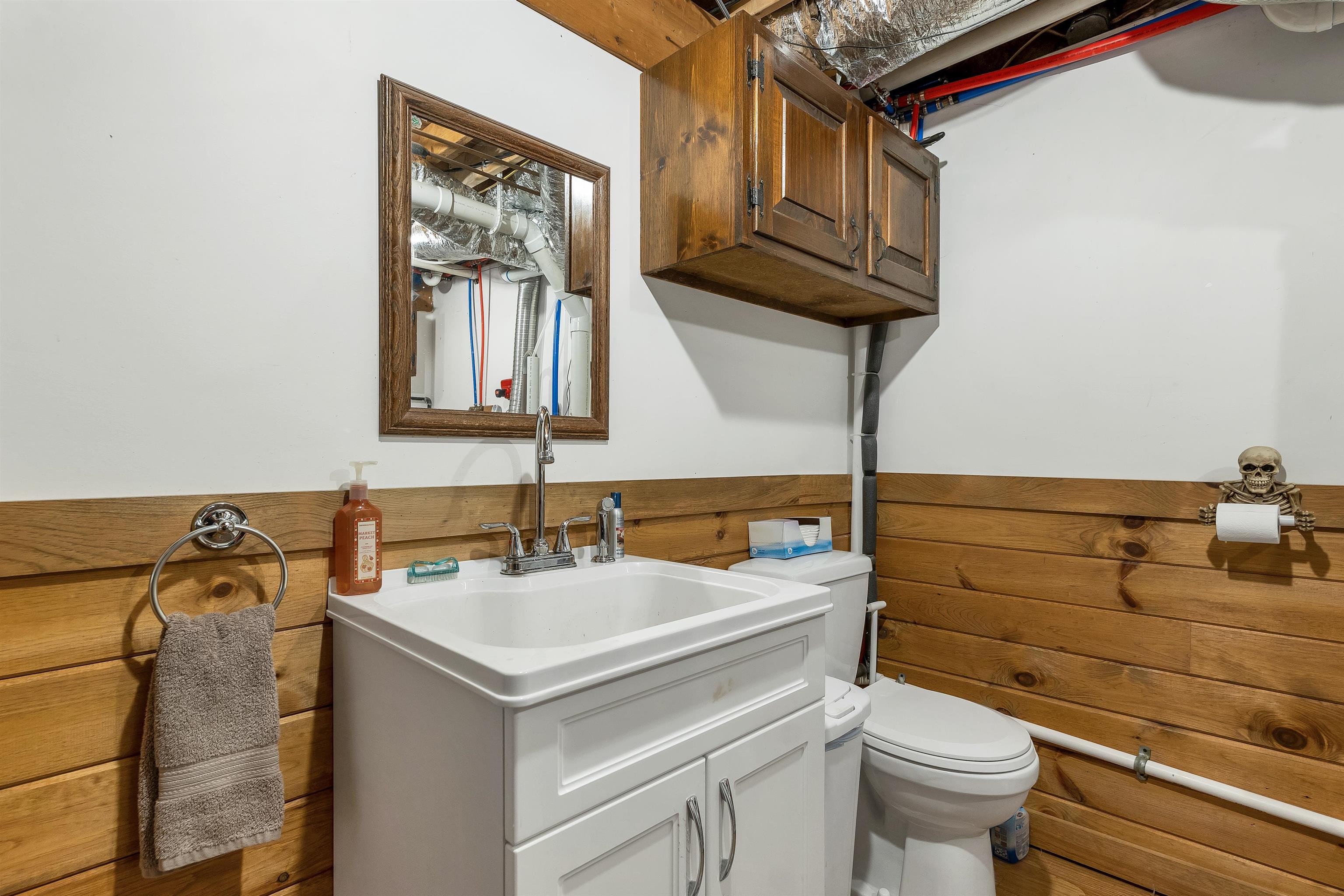 Bathroom with a white vanity and toilet, wood-plank walls, and exposed ceiling plumbing and ductwork.
