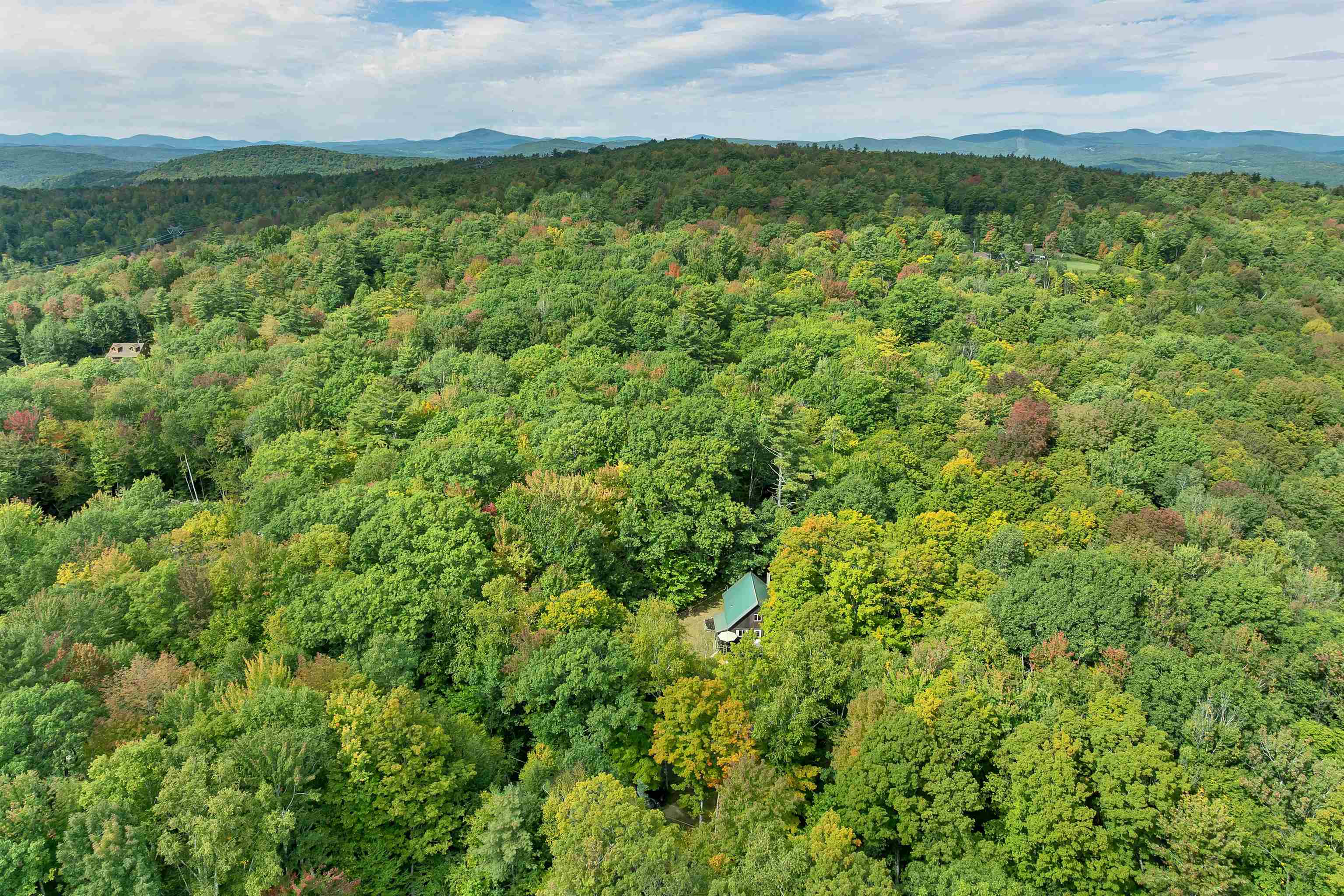 Aerial view of a forest-surrounded house with distant mountain ridges.