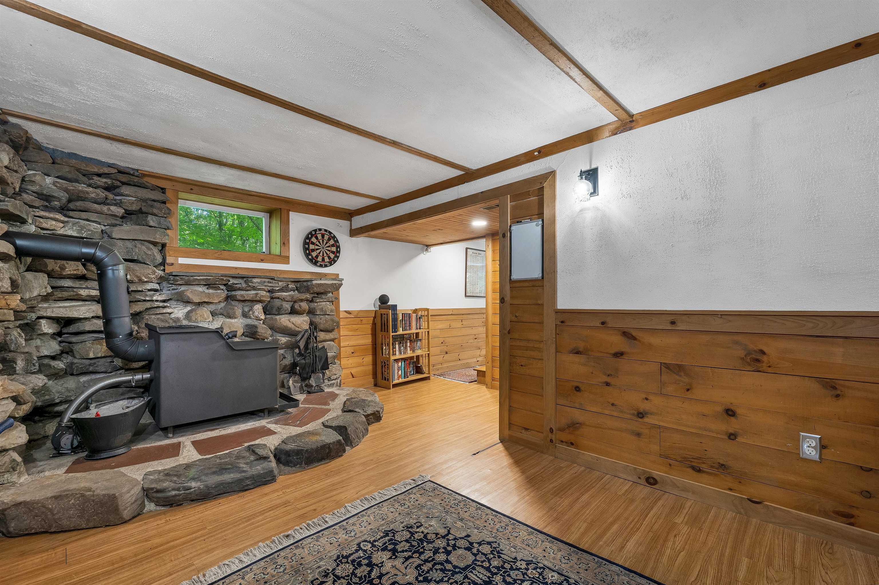Room with a black wood stove set against a stone hearth, timber beams, and wood-paneled walls.