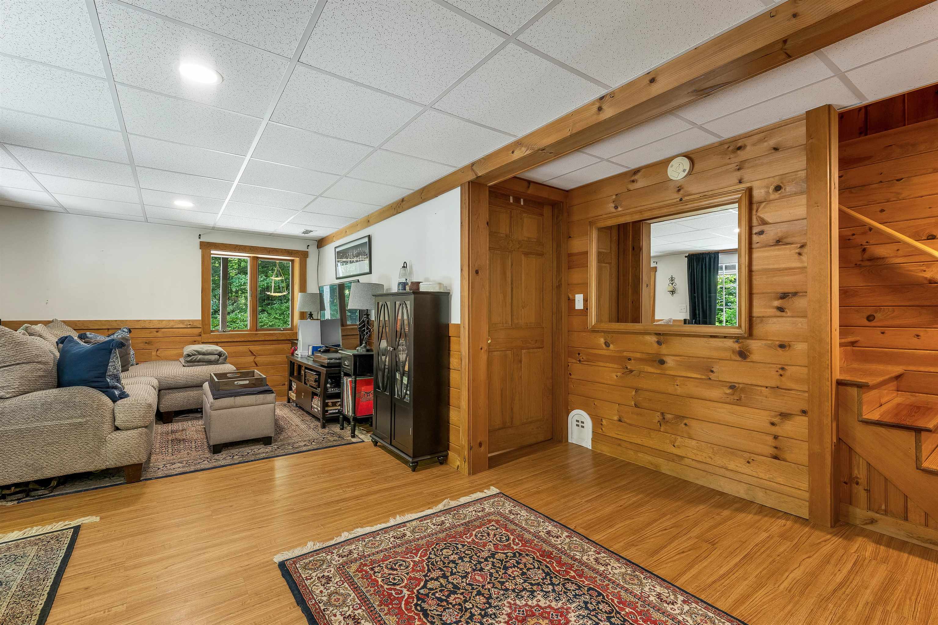 Living room with wood-paneled walls, timber beams, hardwood floors, and a staircase.