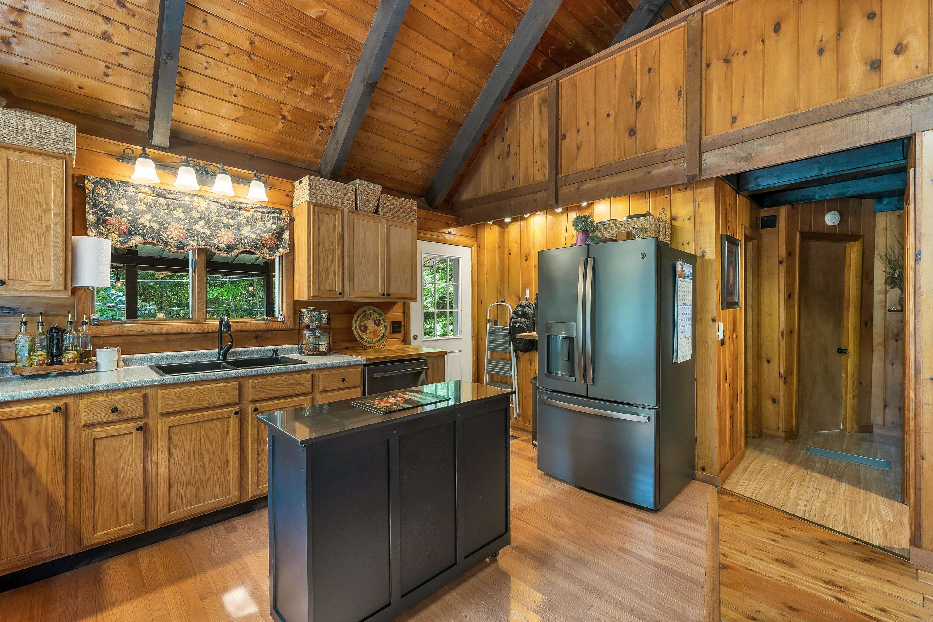 Wood-paneled kitchen with vaulted beam ceiling, dark island, and stainless-steel refrigerator.
