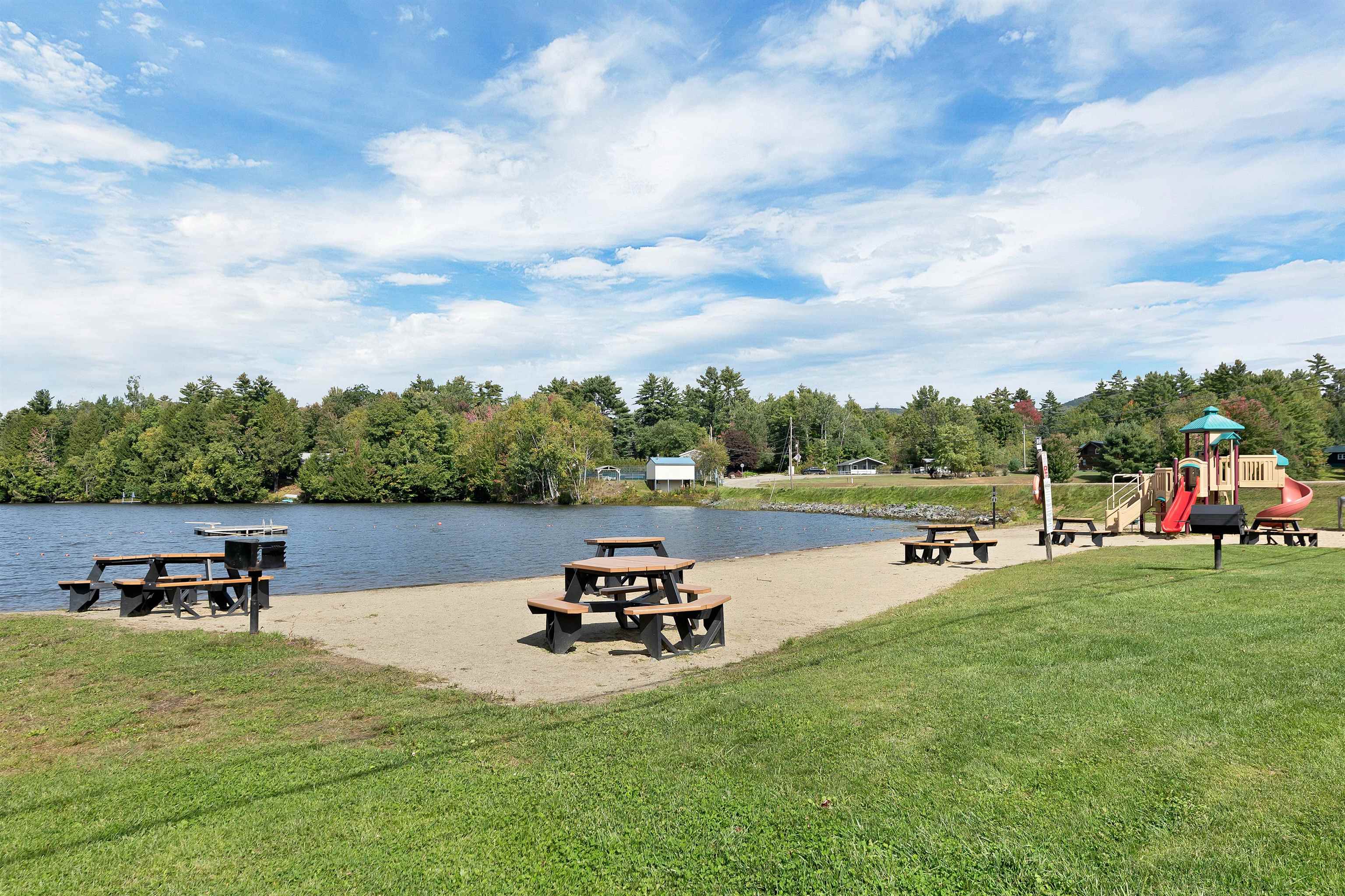 Lakeside beach with picnic tables and a playground beside the water.