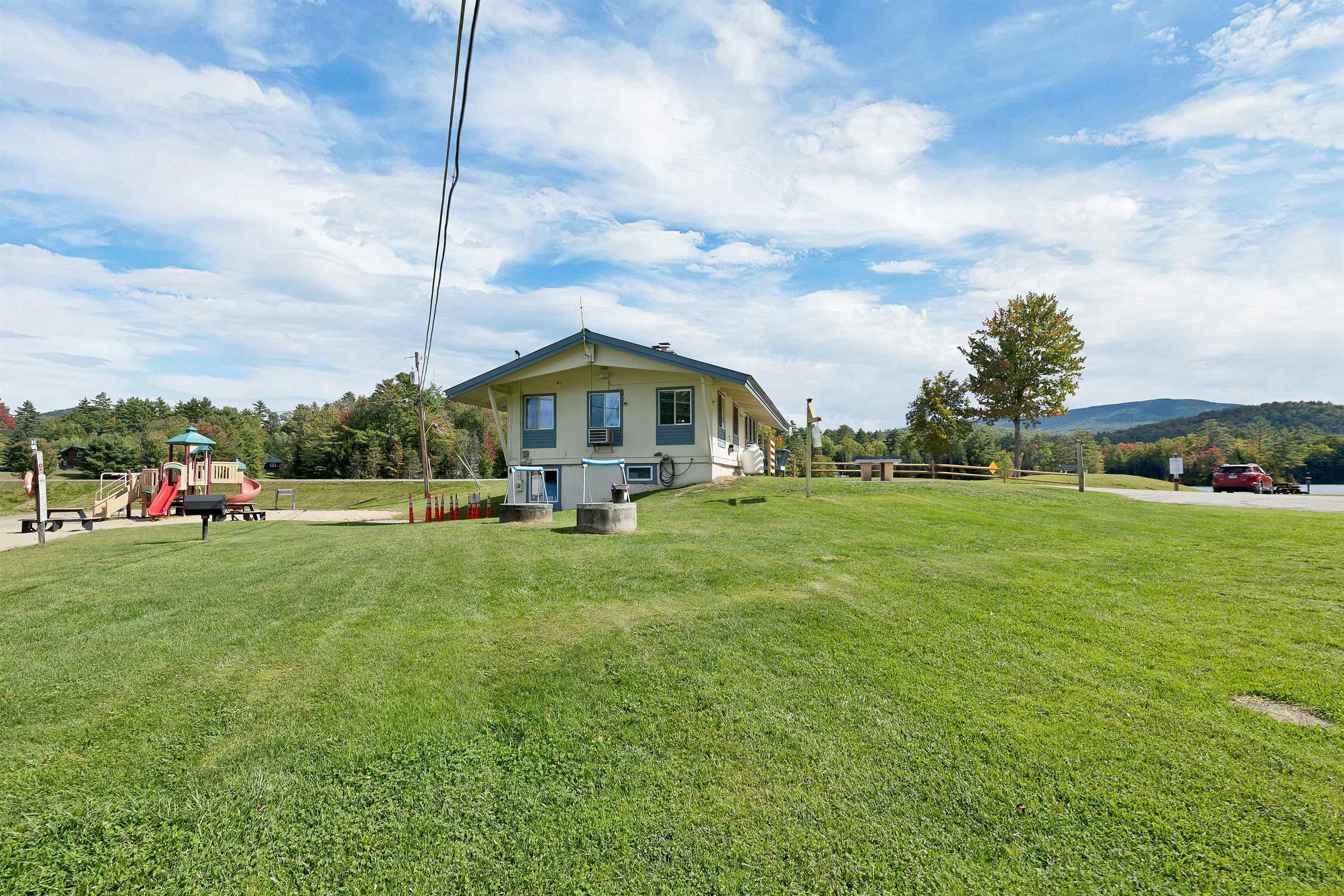 Low building beside a playground on a broad lawn, with a tree-lined mountain ridge in the distance.