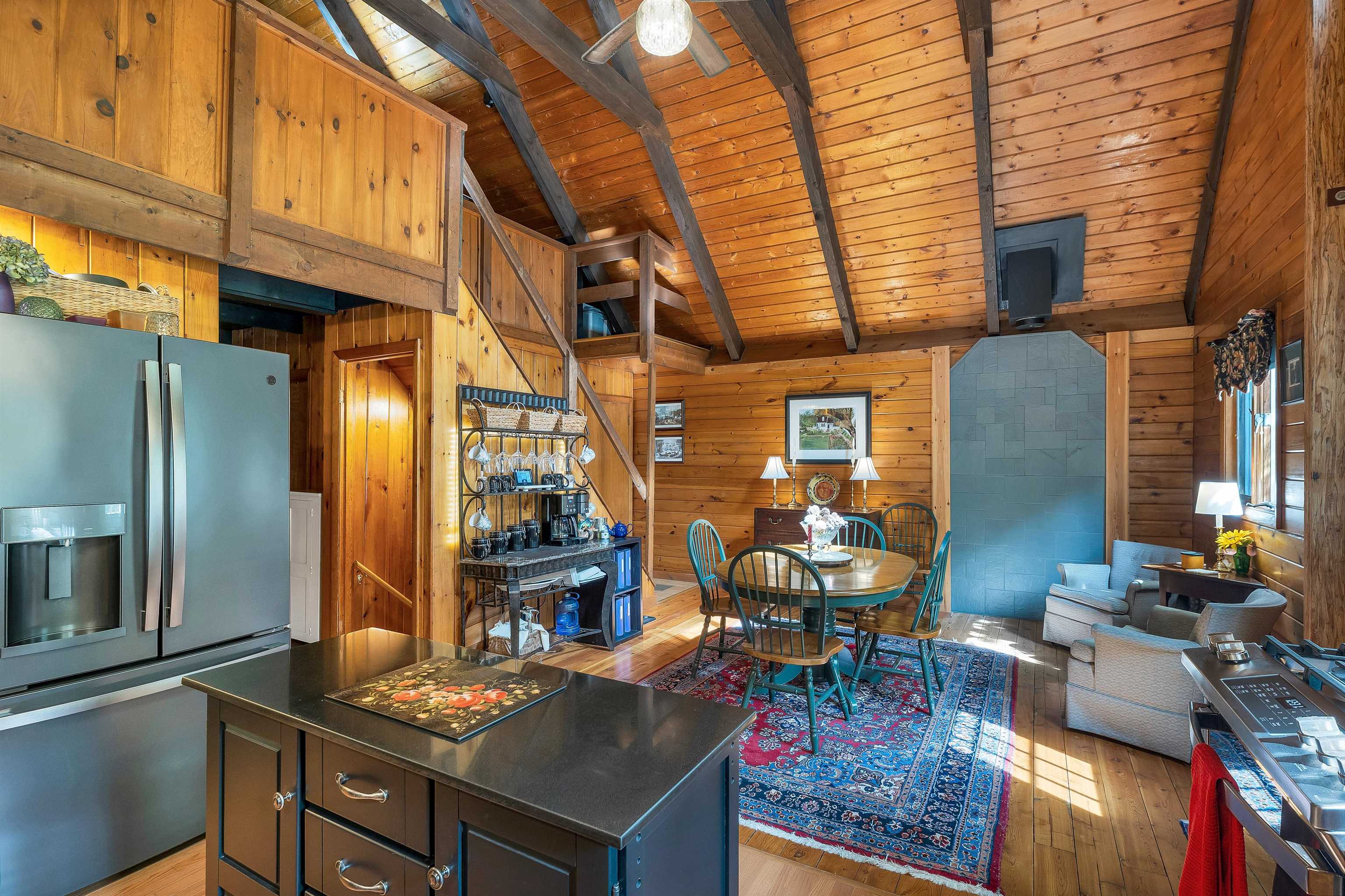 Open-plan kitchen and living area with vaulted wood ceiling, stone fireplace, dining table, and kitchen island.