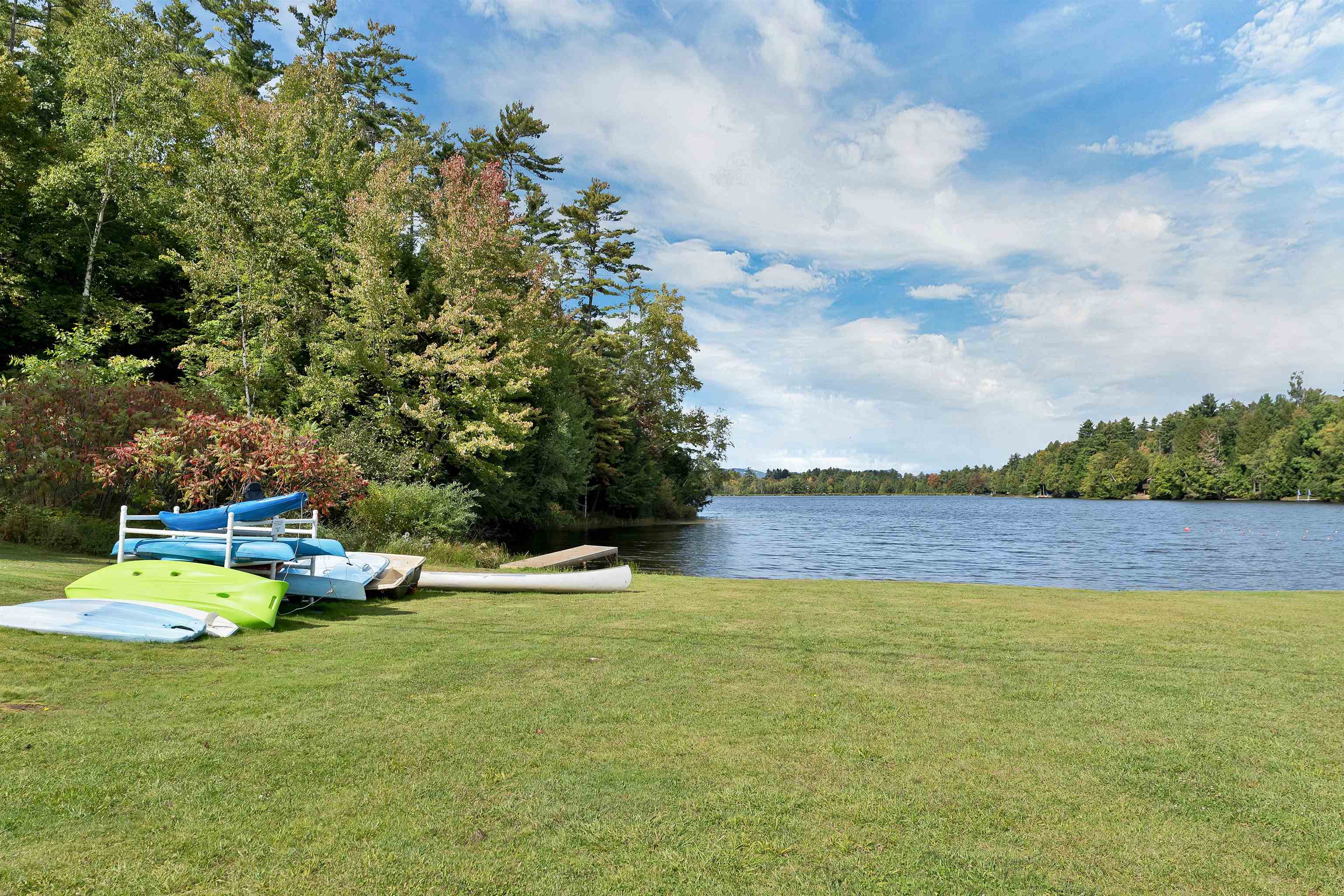 Lakefront lawn with kayaks and canoes beside a calm, tree-lined lake.