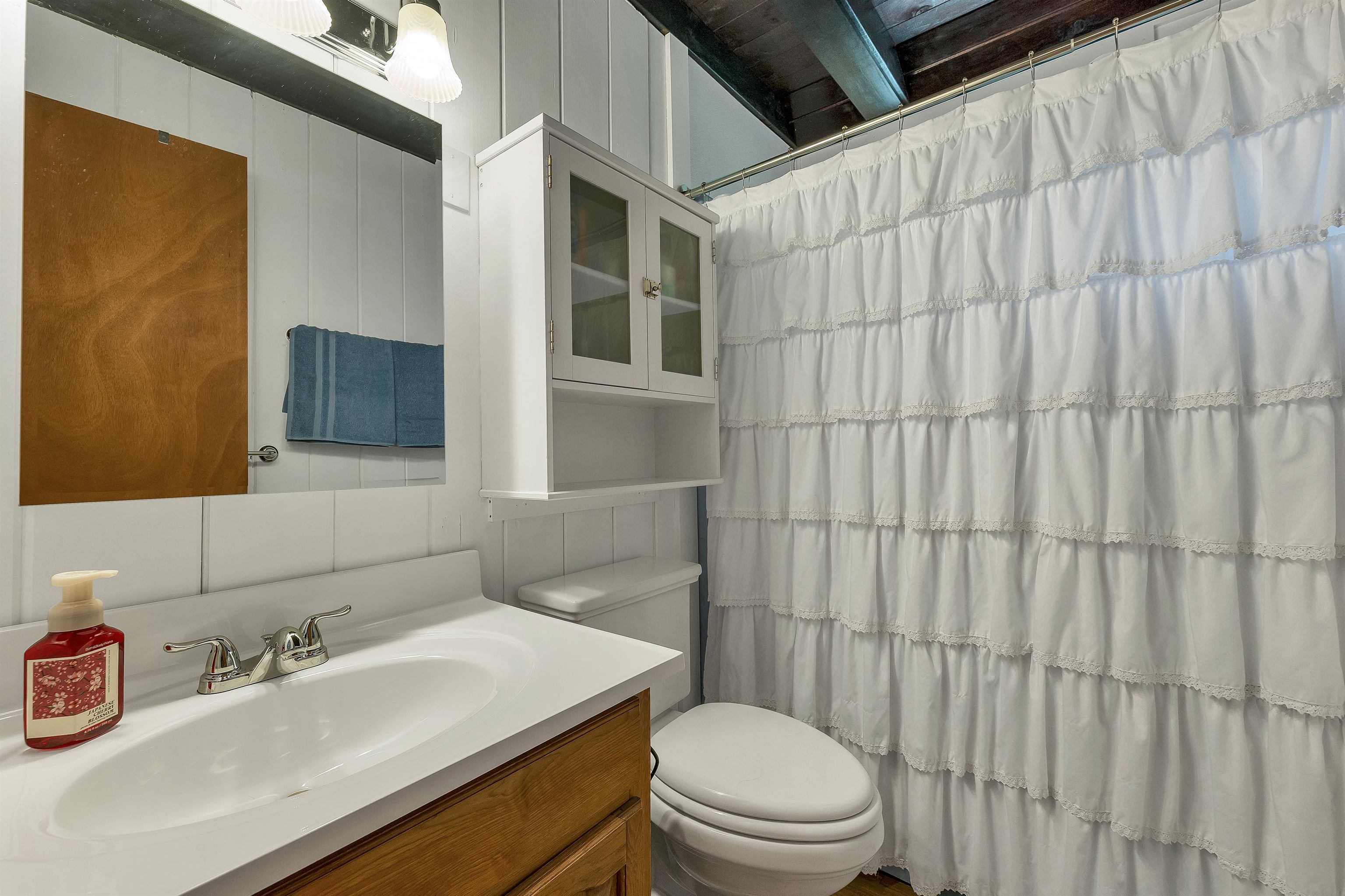 Bathroom with a white vanity, mirrored cabinet, toilet, and tiered white shower curtain.