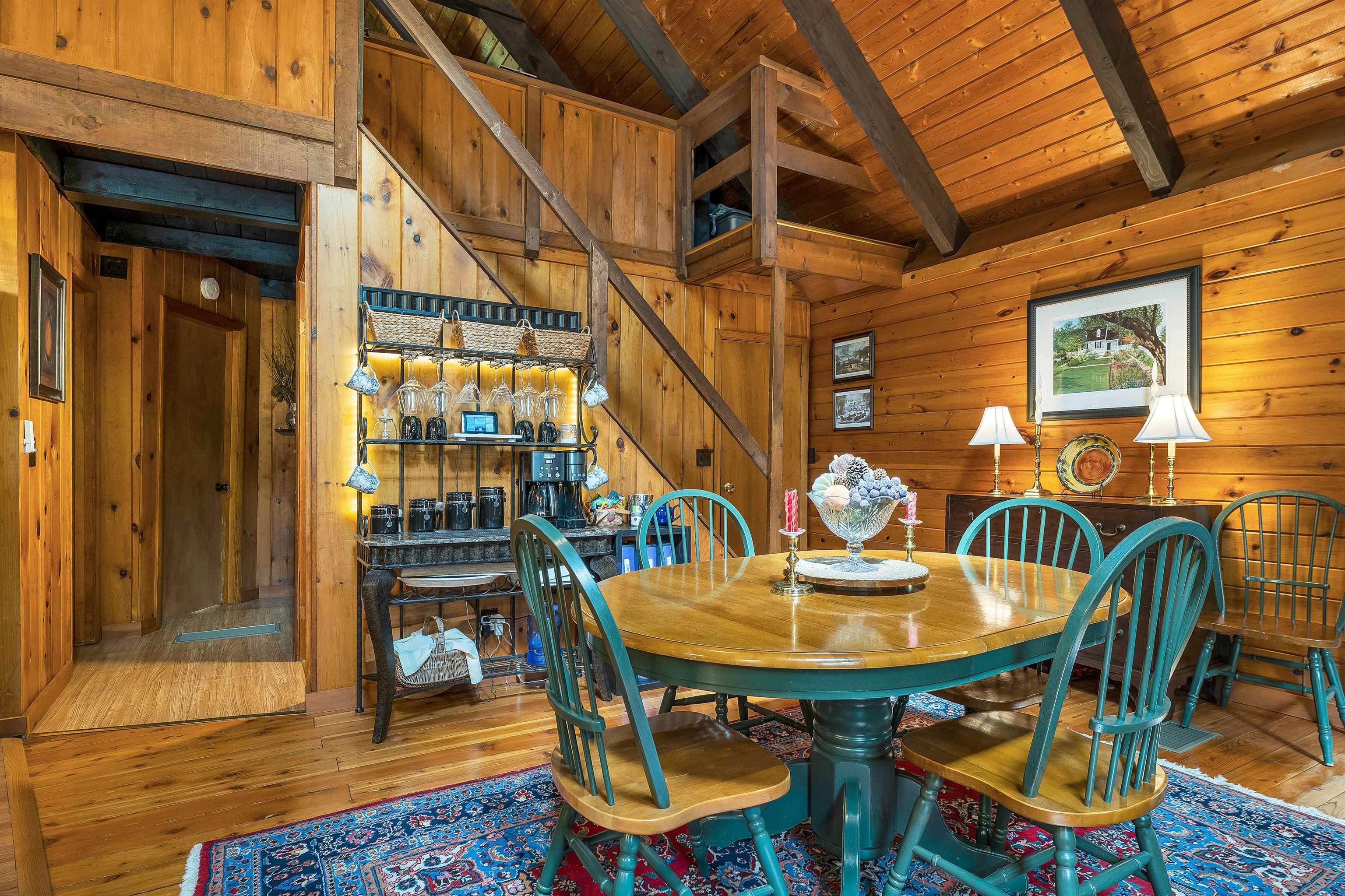 Dining area with a wooden table and teal chairs beneath exposed beams in a knotty-pine interior.