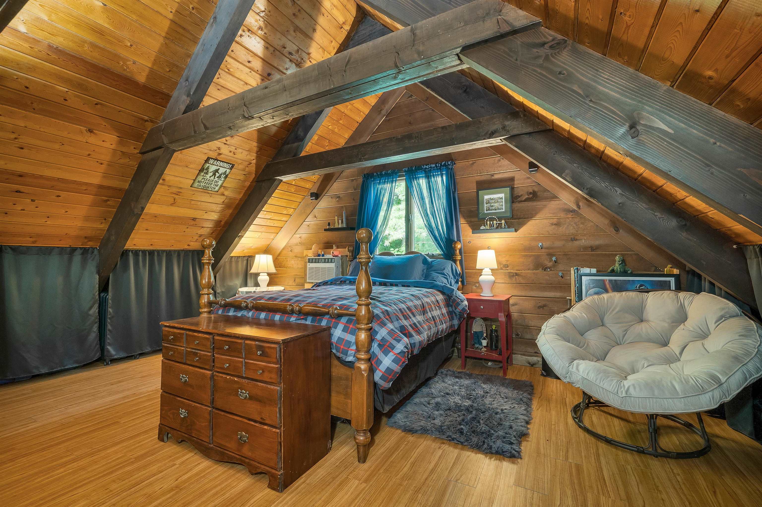 Attic bedroom with exposed timber beams, a four-poster bed, and a round cushioned chair.
