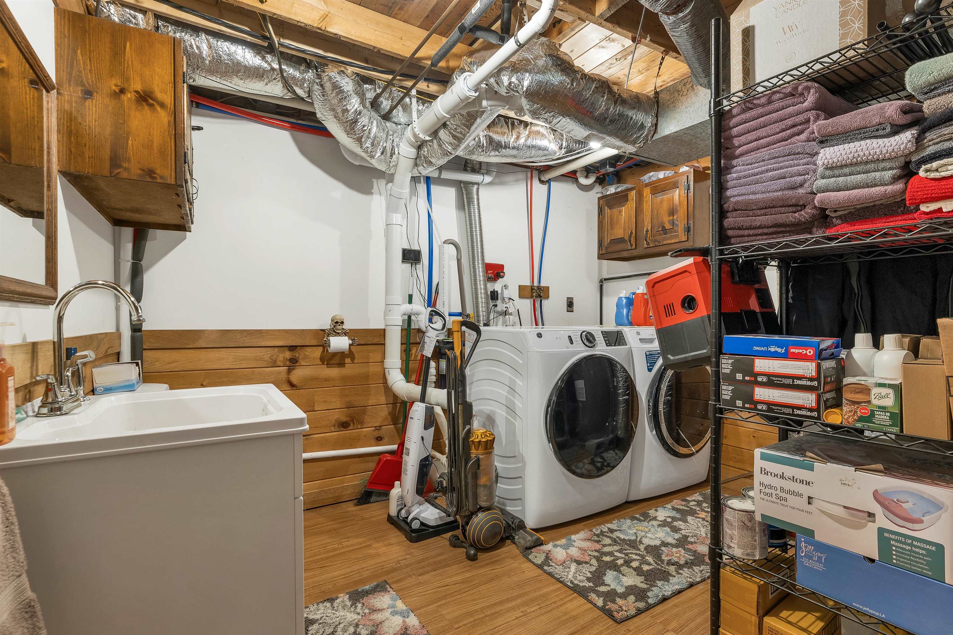 Basement laundry room with front-loading washer and dryer, deep utility sink, and exposed ductwork.