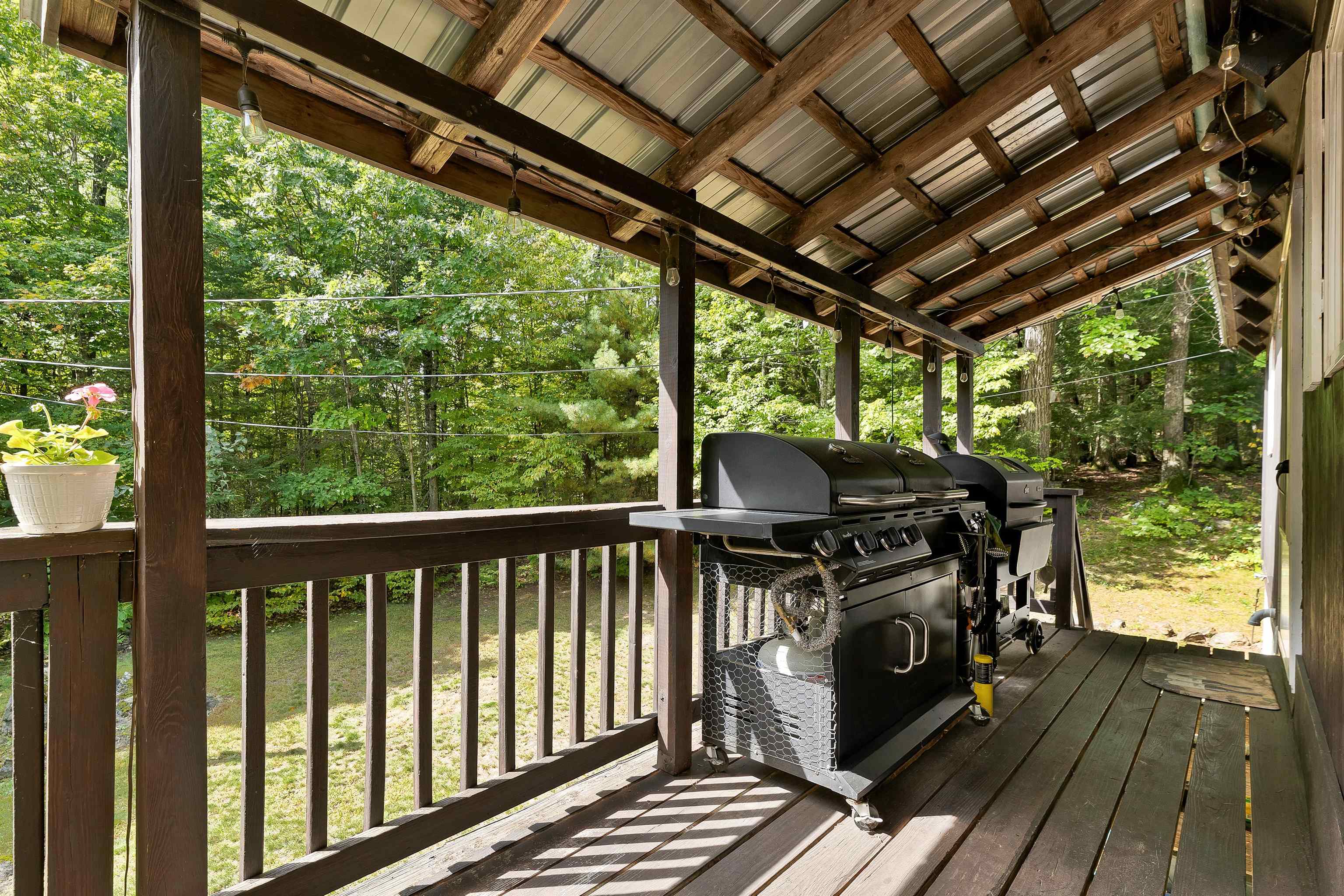 Covered wooden deck with several grills overlooking a leafy wooded yard.