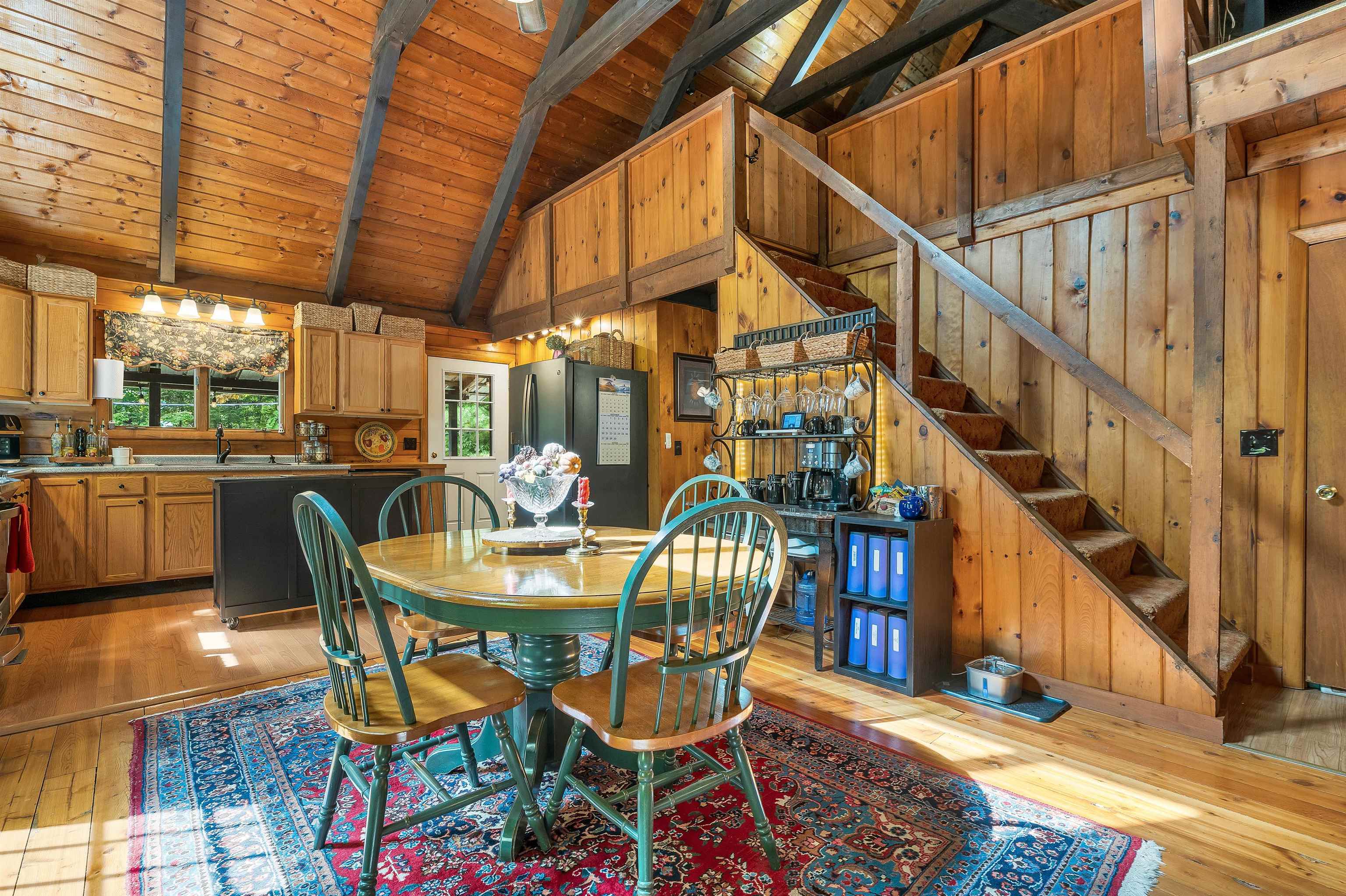 Wood-paneled kitchen and dining area with a vaulted ceiling, patterned rug, and staircase.