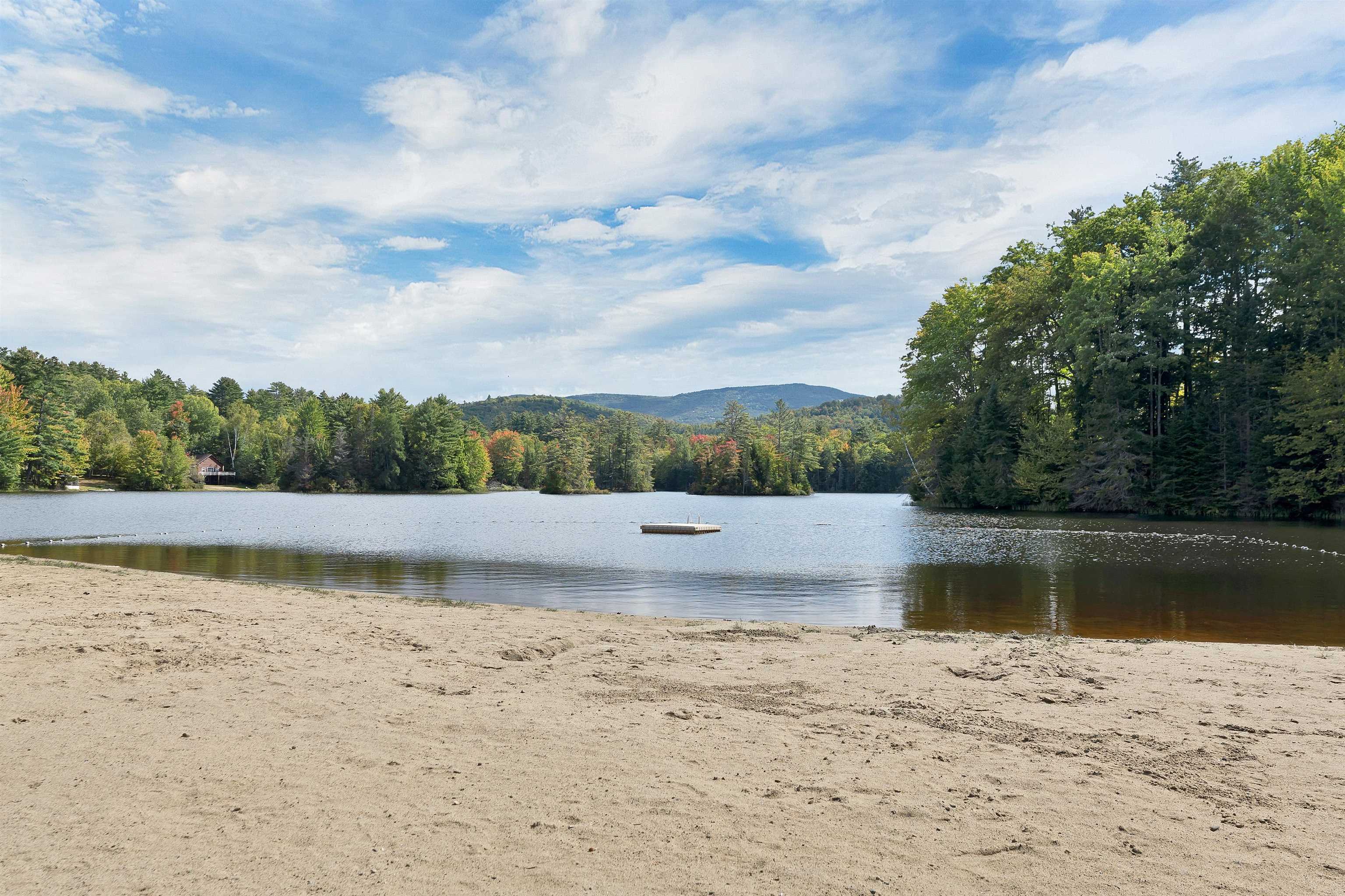 Sandy lakeside beach with a floating dock and wooded shoreline.