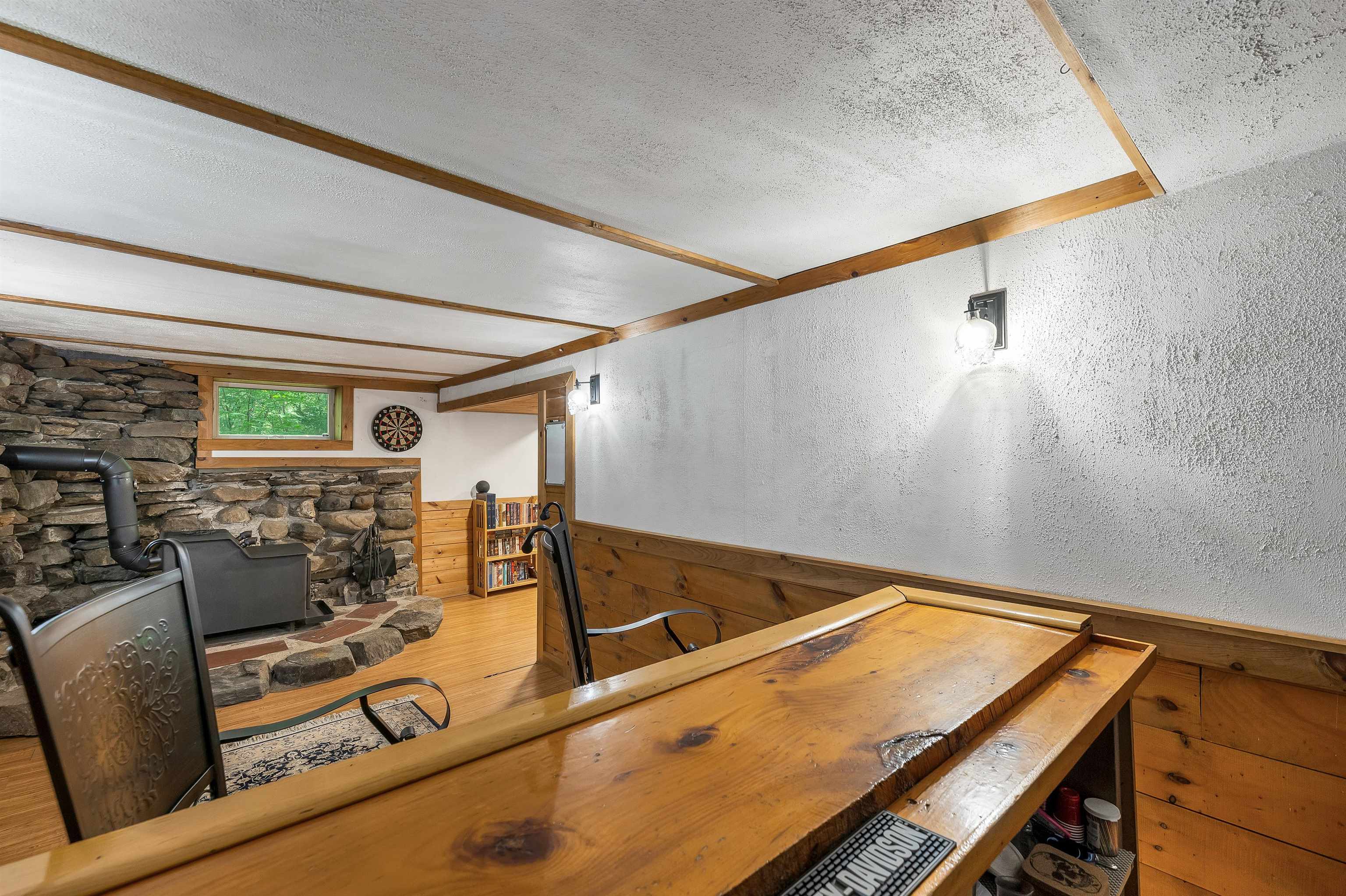 Basement recreation room with a wooden bar, stone fireplace wall, wood stove, and dartboard.
