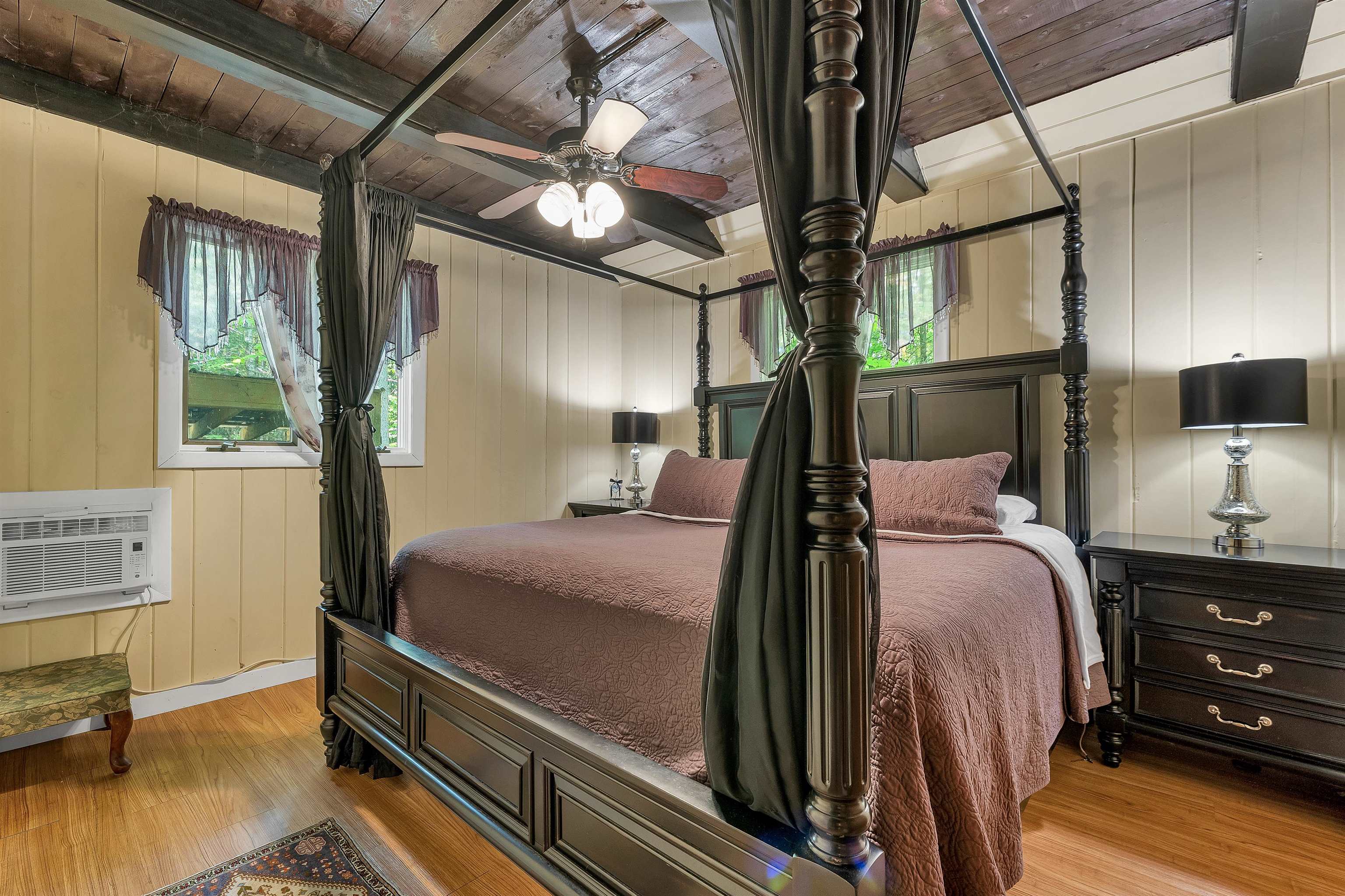 Bedroom with a dark four-poster bed, mauve bedding, and a wood-plank ceiling.