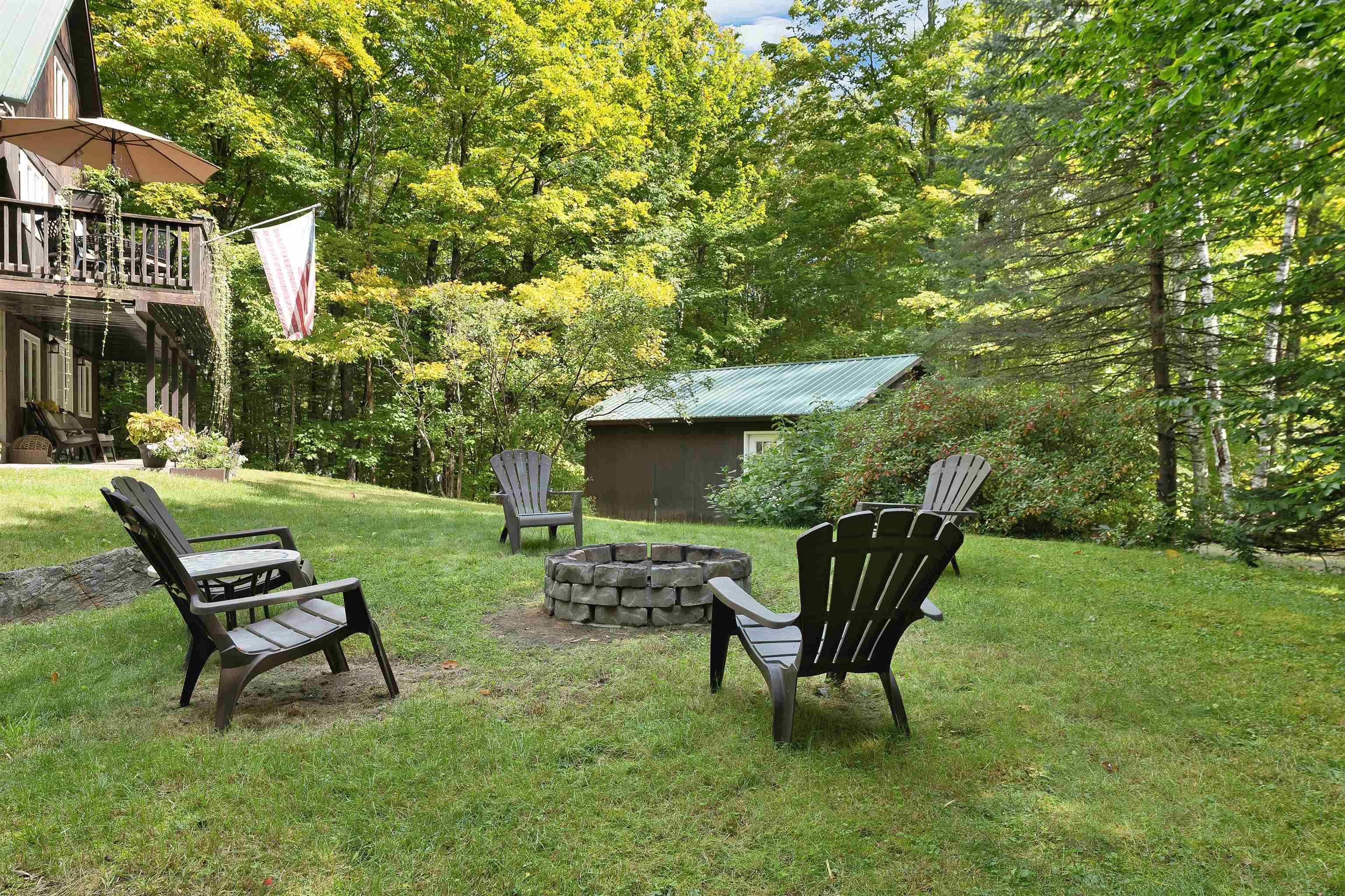 Wooded backyard with Adirondack chairs around a stone fire pit, a raised deck, and a shed.