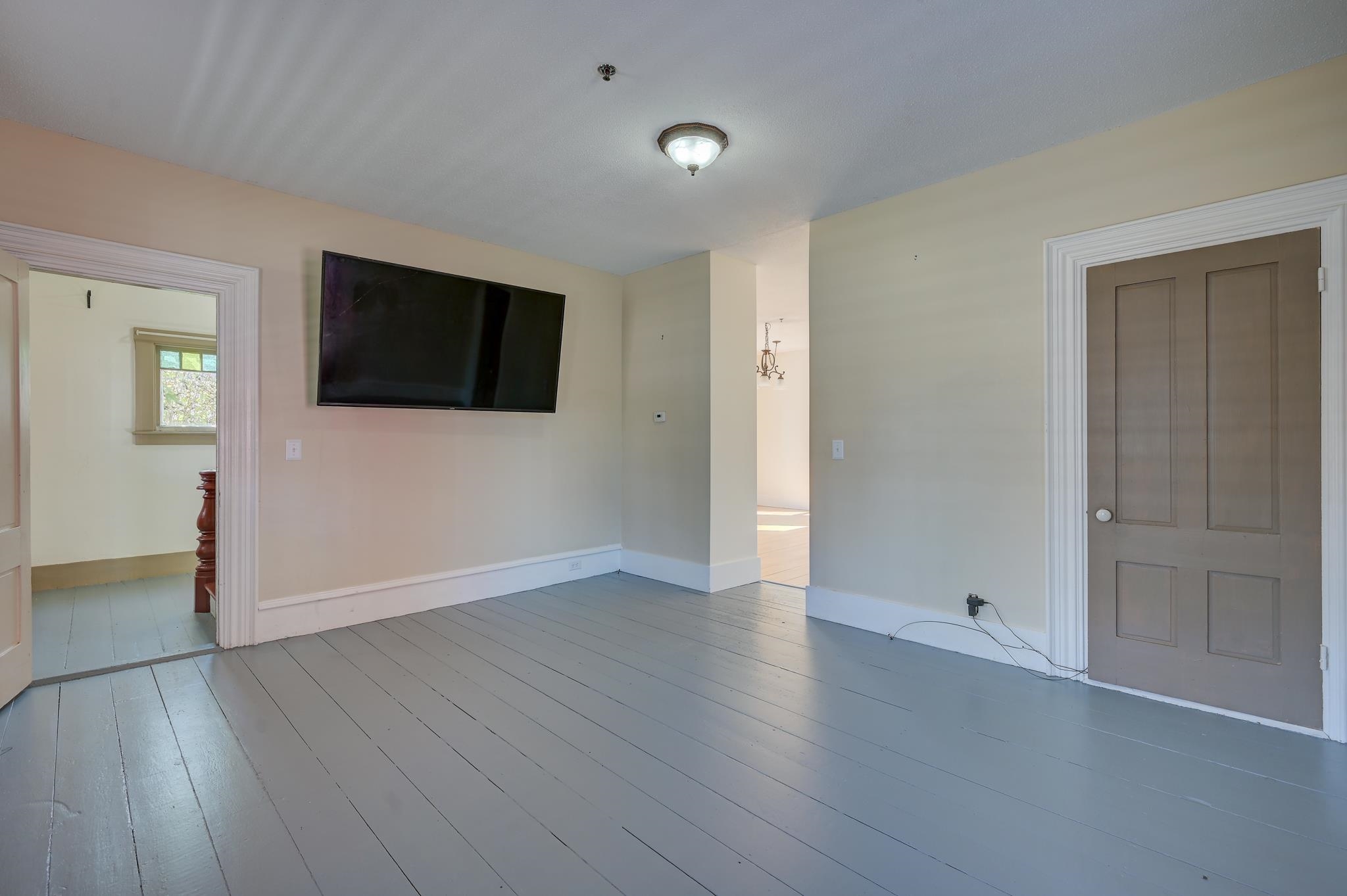 Room with gray plank flooring, a wall-mounted television, and a brown paneled door.