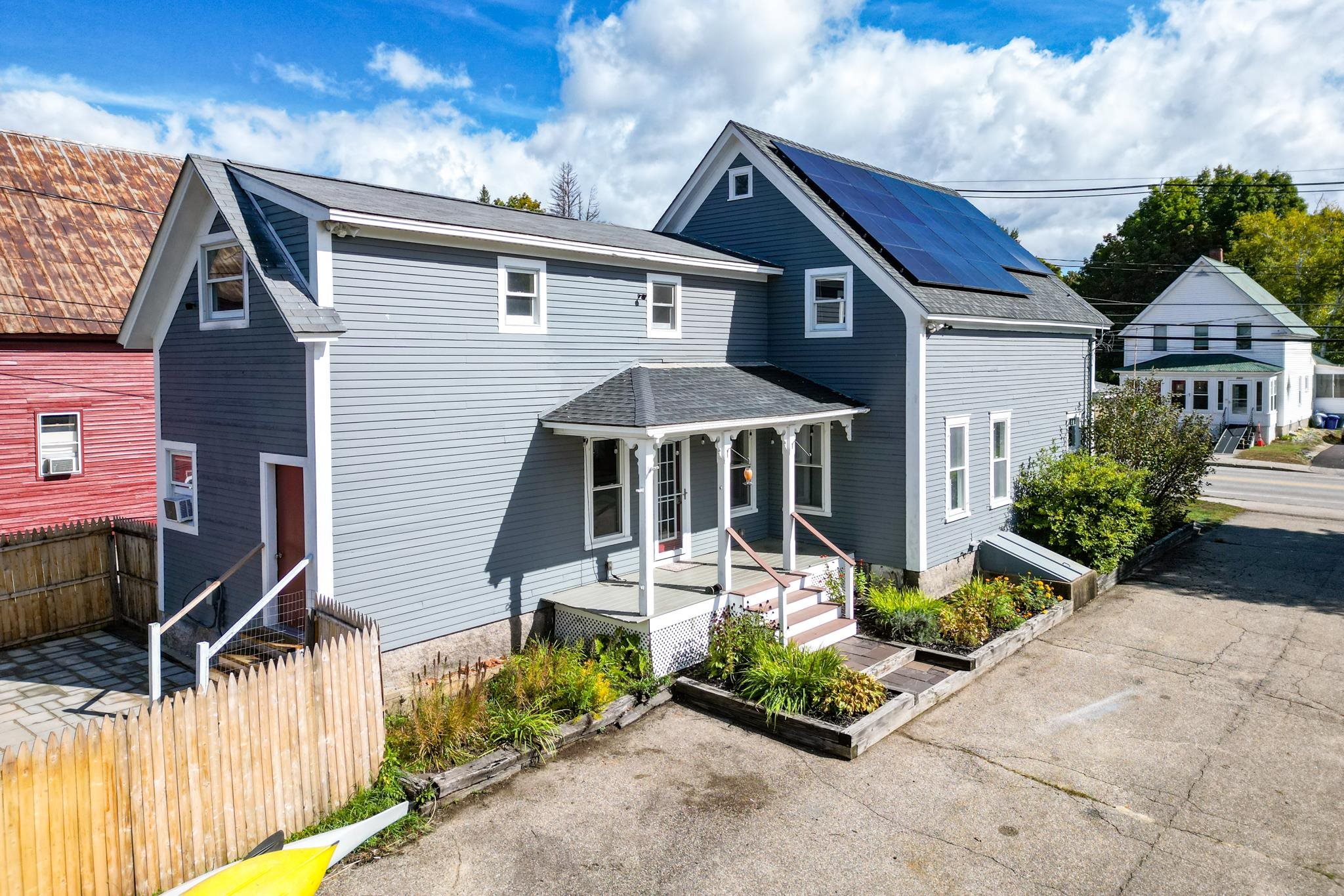 Gray two-story home with a covered porch, rooftop solar panels, and garden beds beside the driveway.