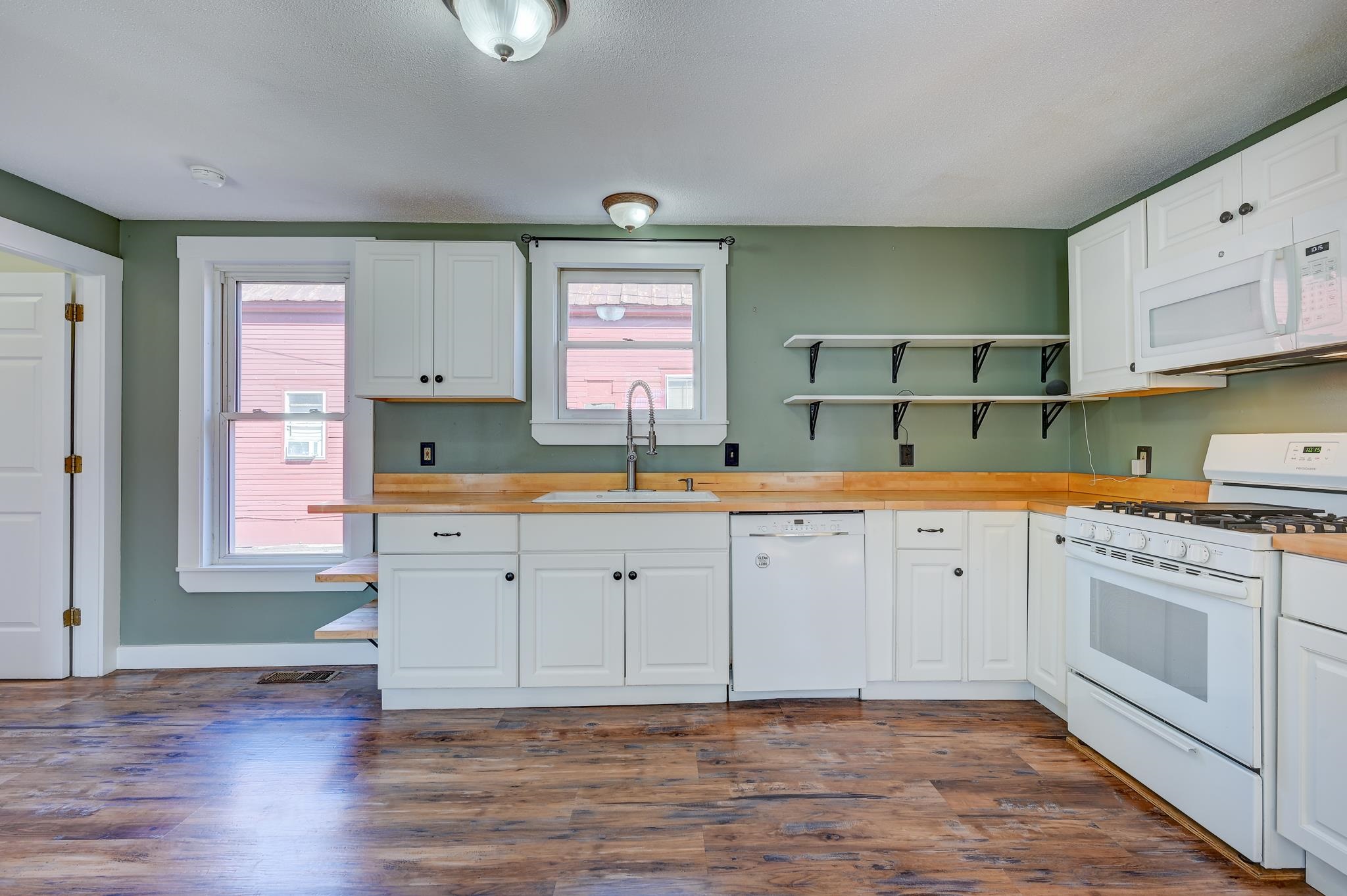 Kitchen with white cabinets, wood countertops and floors, green walls, and windows overlooking a pink building.