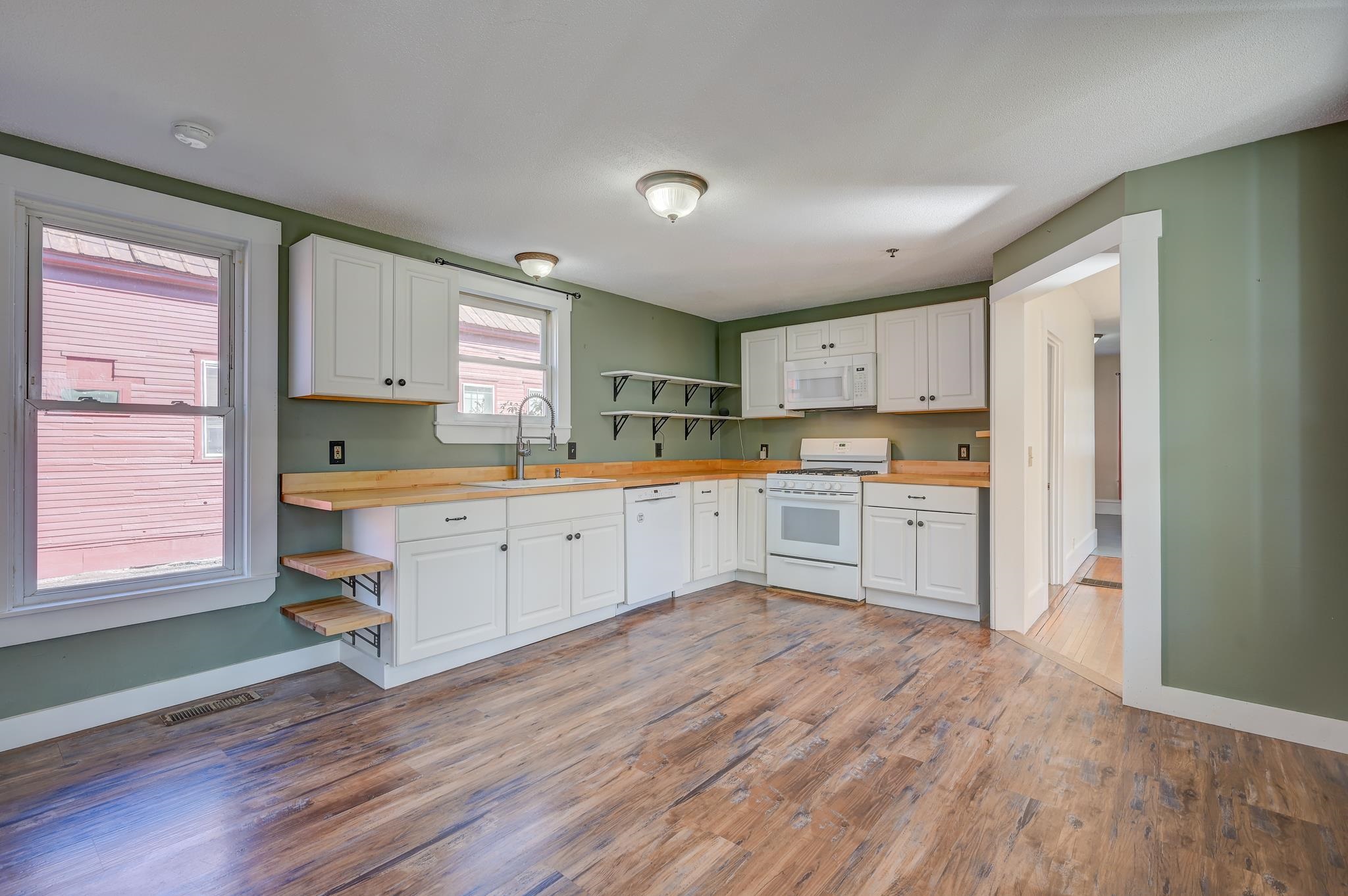 Vacant kitchen with white cabinets, wood countertops, open shelves, and sage-green walls.