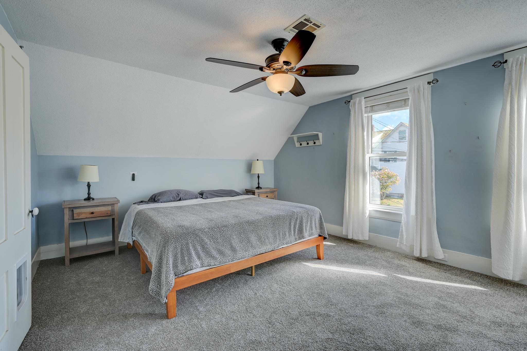 Furnished bedroom with a sloped ceiling, gray bedding, blue-gray walls, and a curtained window.