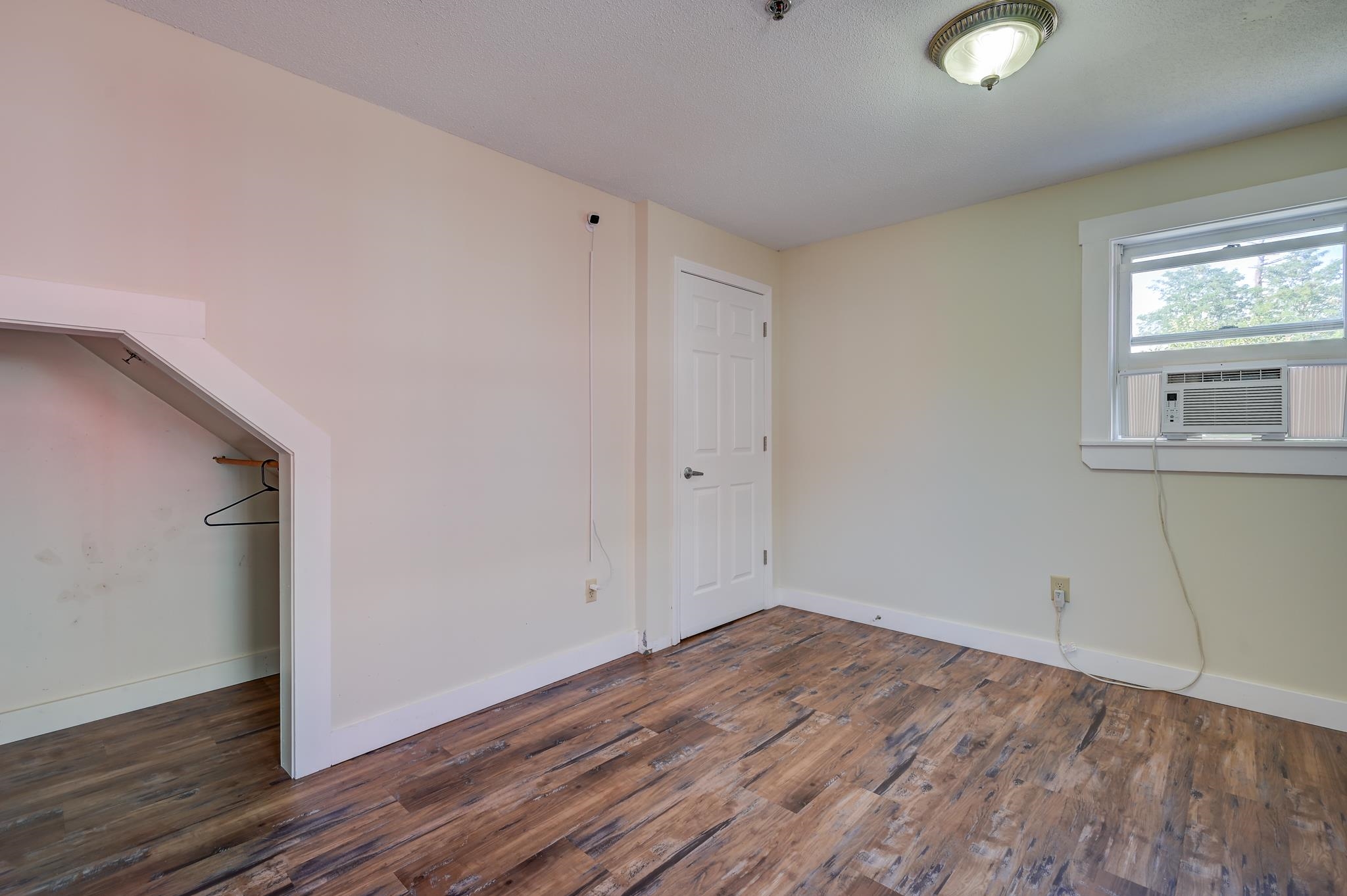 Empty bedroom with wood-look flooring, an open closet, and a window air conditioner.