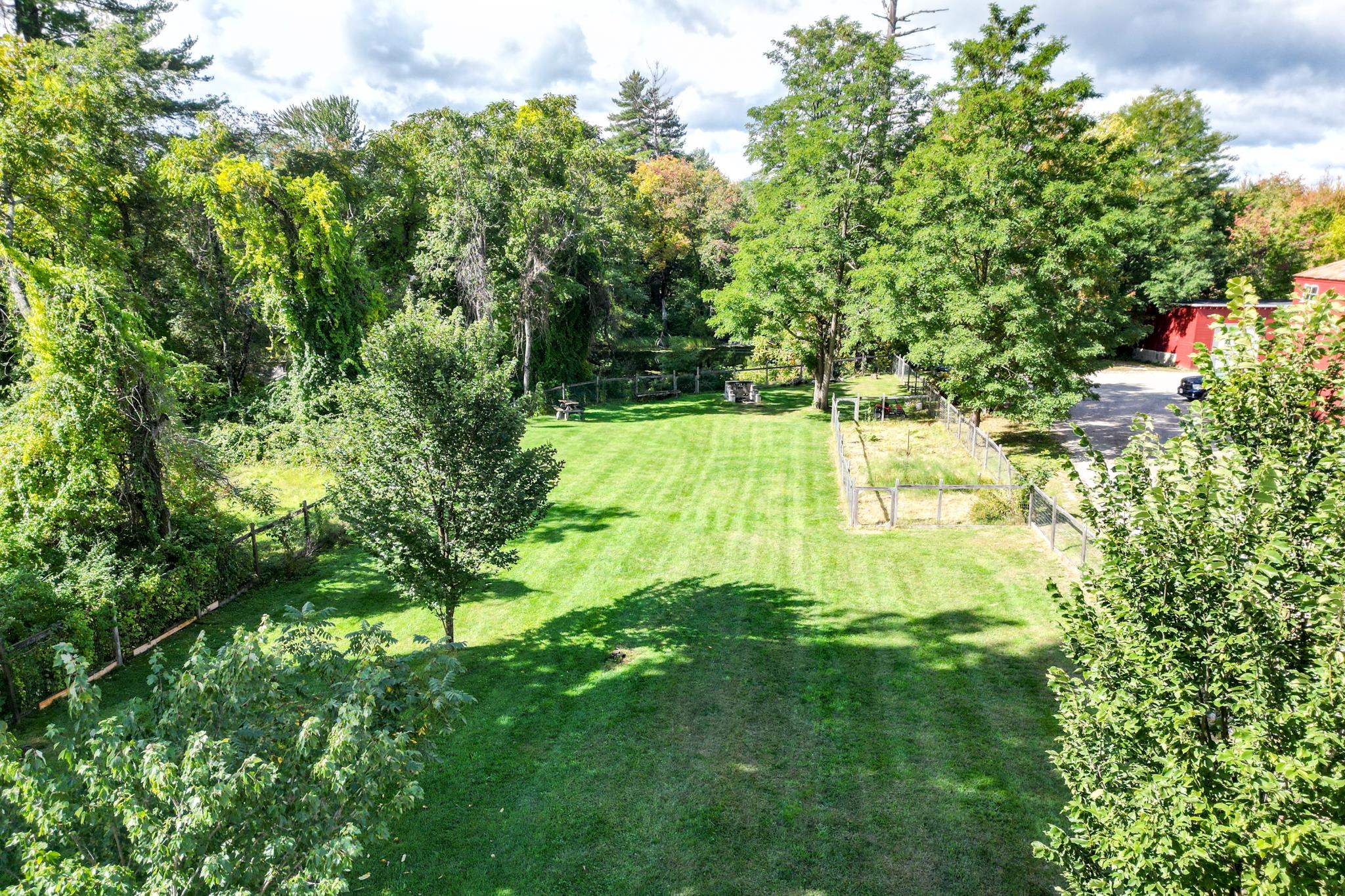 Property grounds with a broad lawn, wooded borders, fenced garden areas, and a red outbuilding.