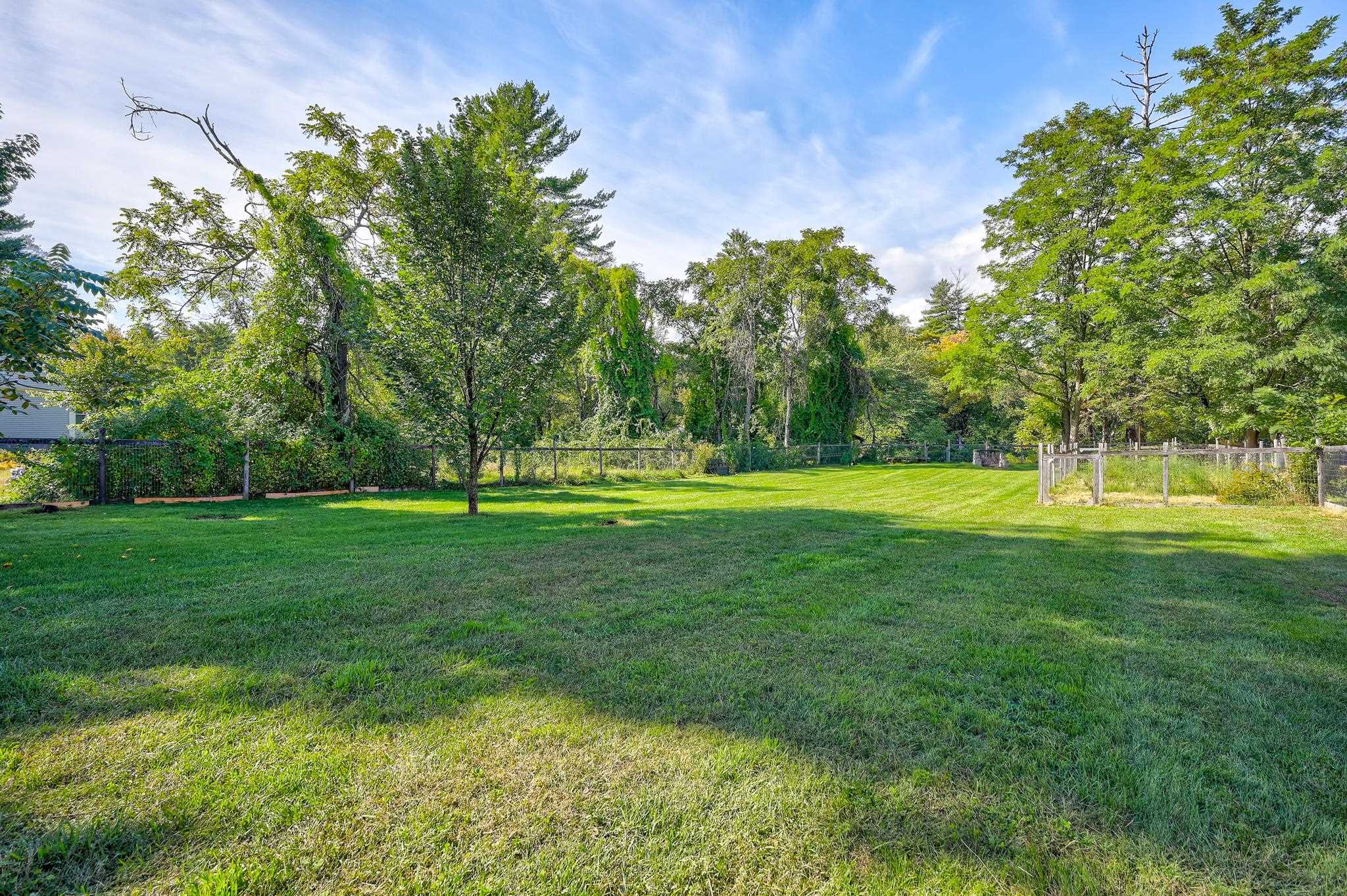 Spacious grassy backyard with mature trees, perimeter fencing, and a small fenced garden.