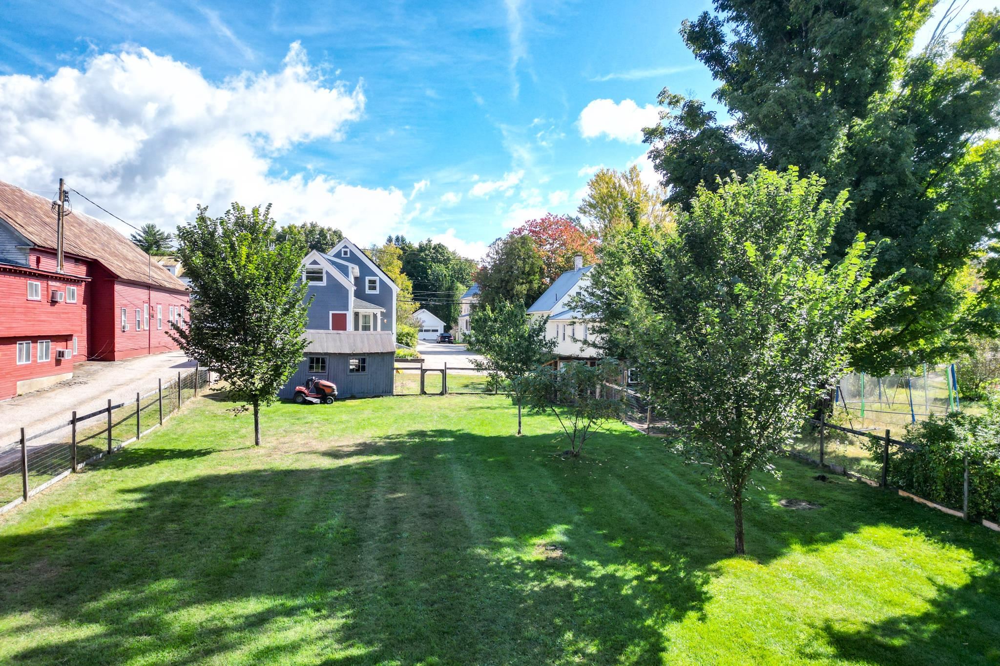 Fenced backyard with a broad lawn, leafy trees, and a small shed.