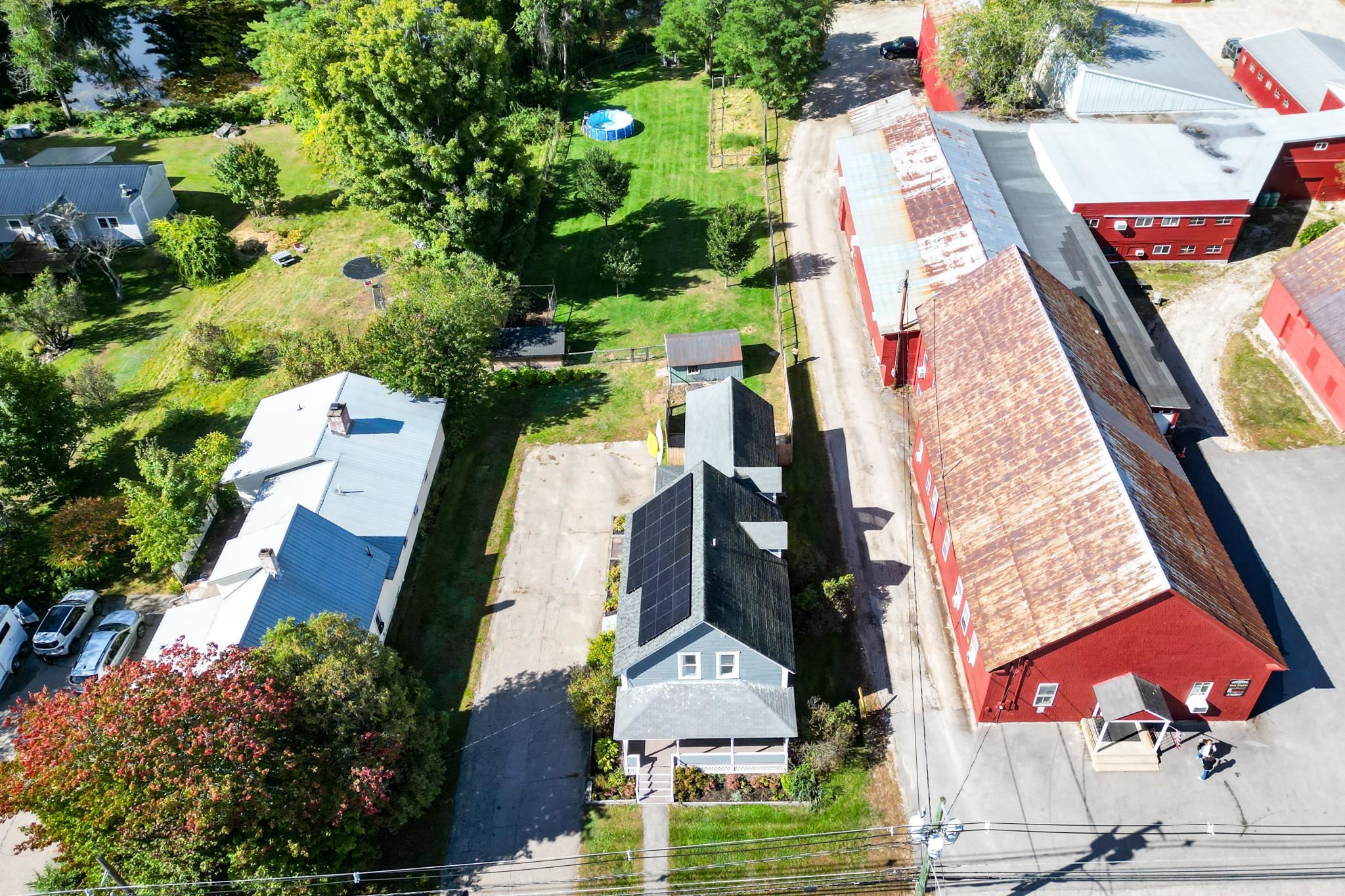Gray house with rooftop solar panels and covered porch beside a large red commercial building.