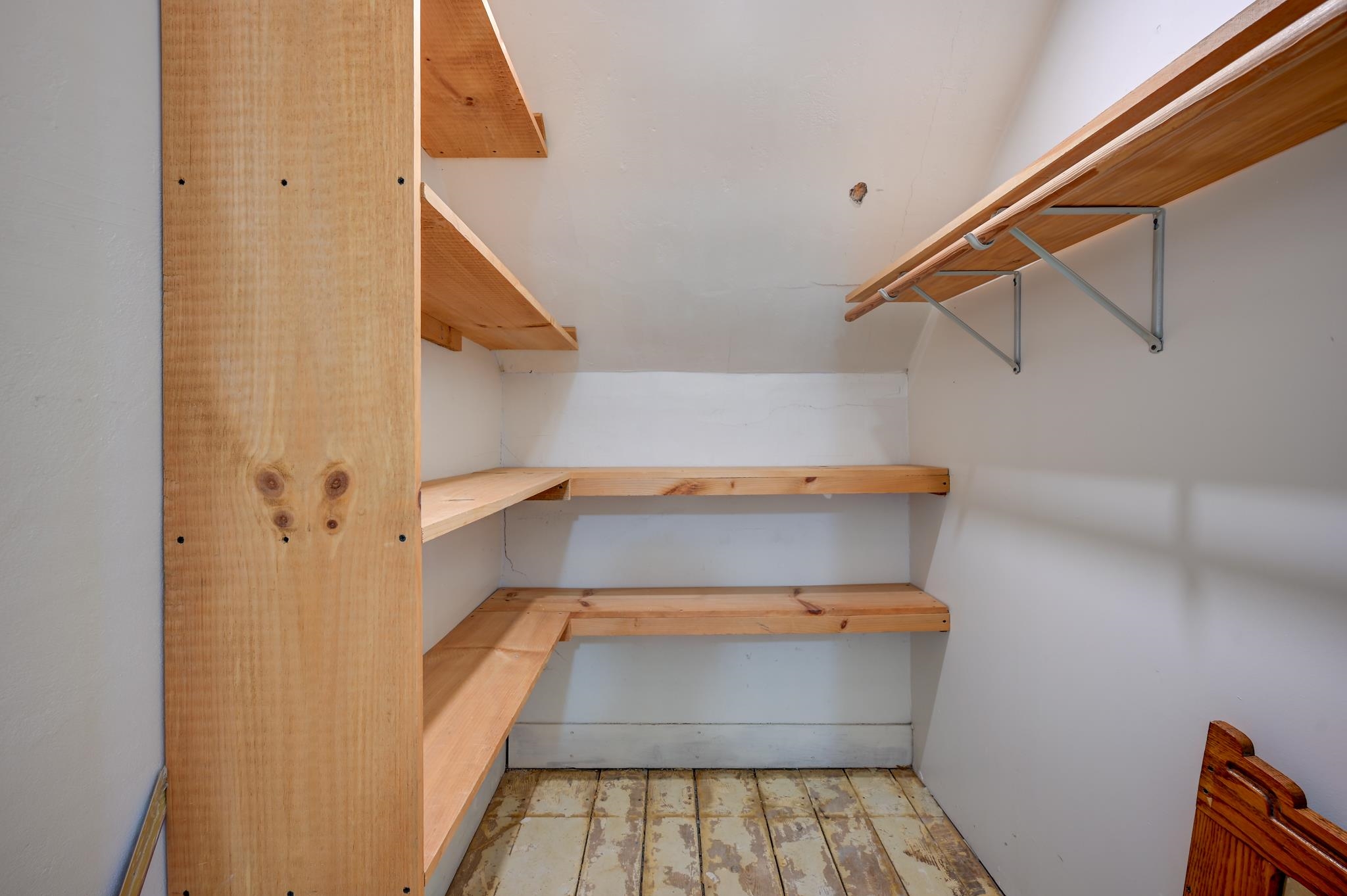 Empty closet with built-in wooden shelves, a hanging rod, and worn plank flooring.
