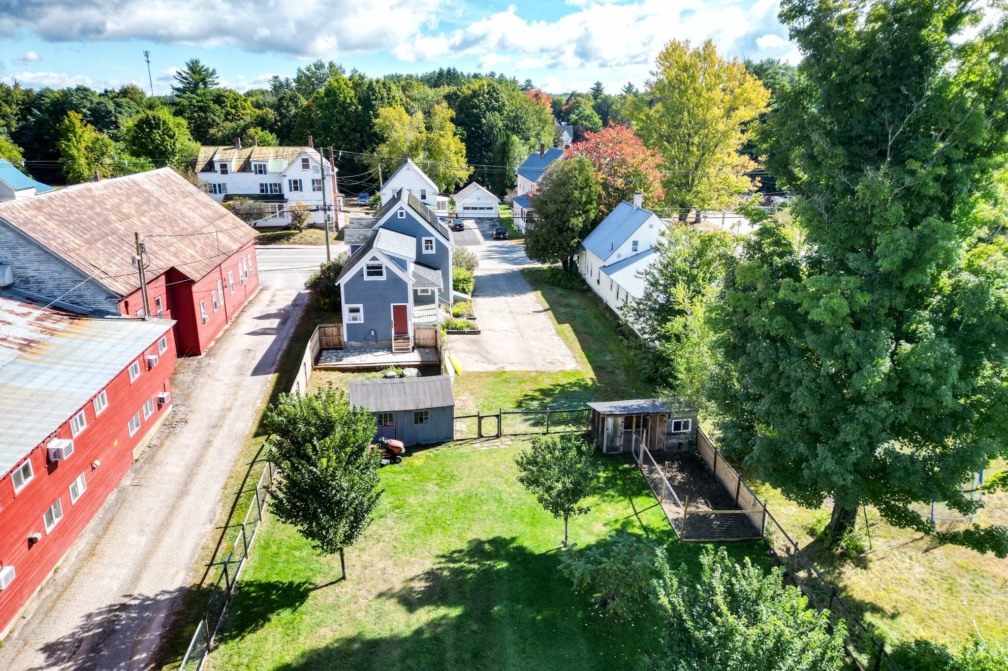 Aerial view of a blue house, fenced lawn, sheds, and surrounding neighborhood.