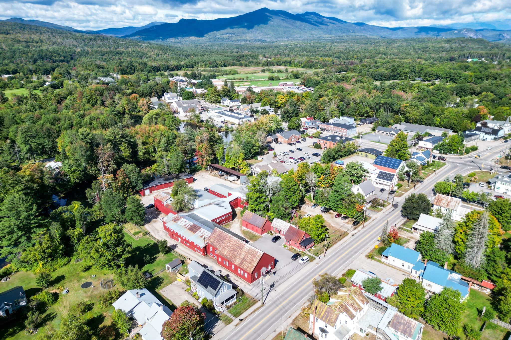 Aerial view of a village beside wooded mountains, with red barns along the main road.
