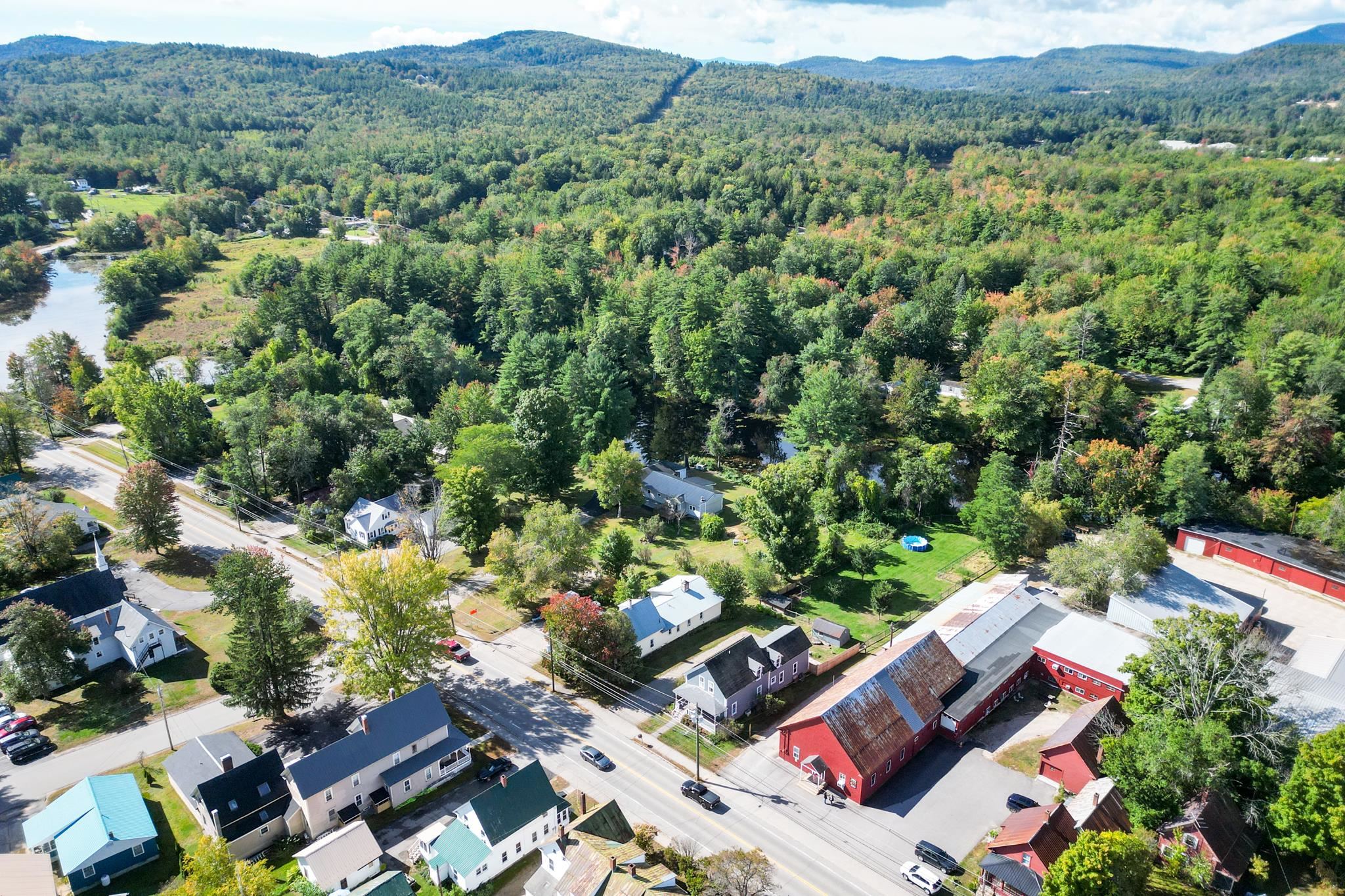 Aerial view of Conway homes and a red barn, with a river and forested hills beyond.