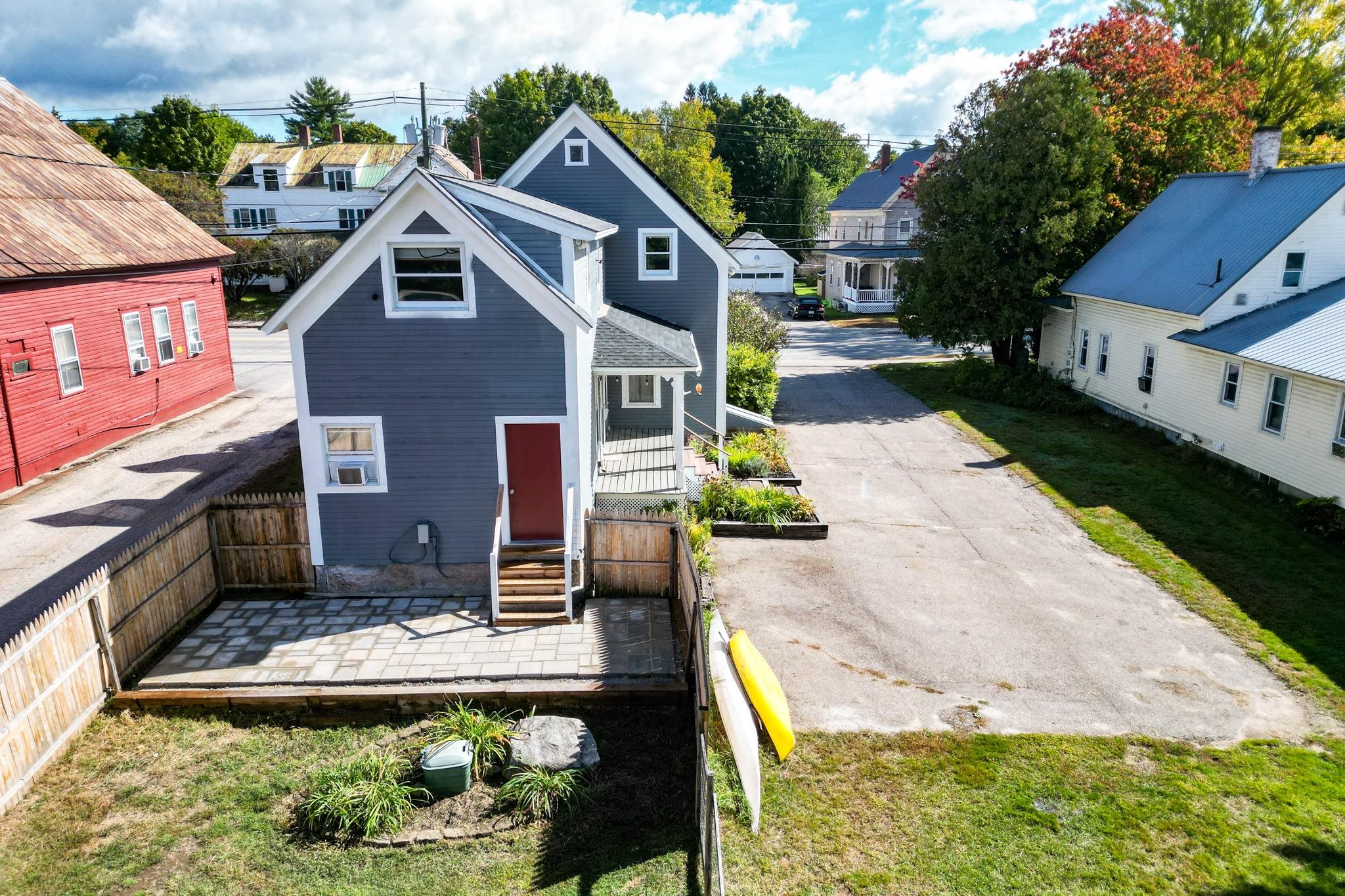 Gray-blue house with a red door and fenced stone-paver patio, viewed from above.