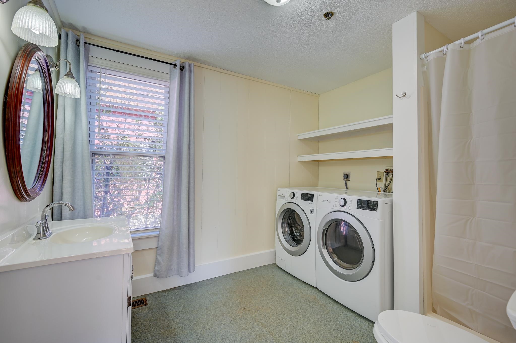 Laundry room with front-loading washer and dryer, open shelves, a sink, and a curtained shower.