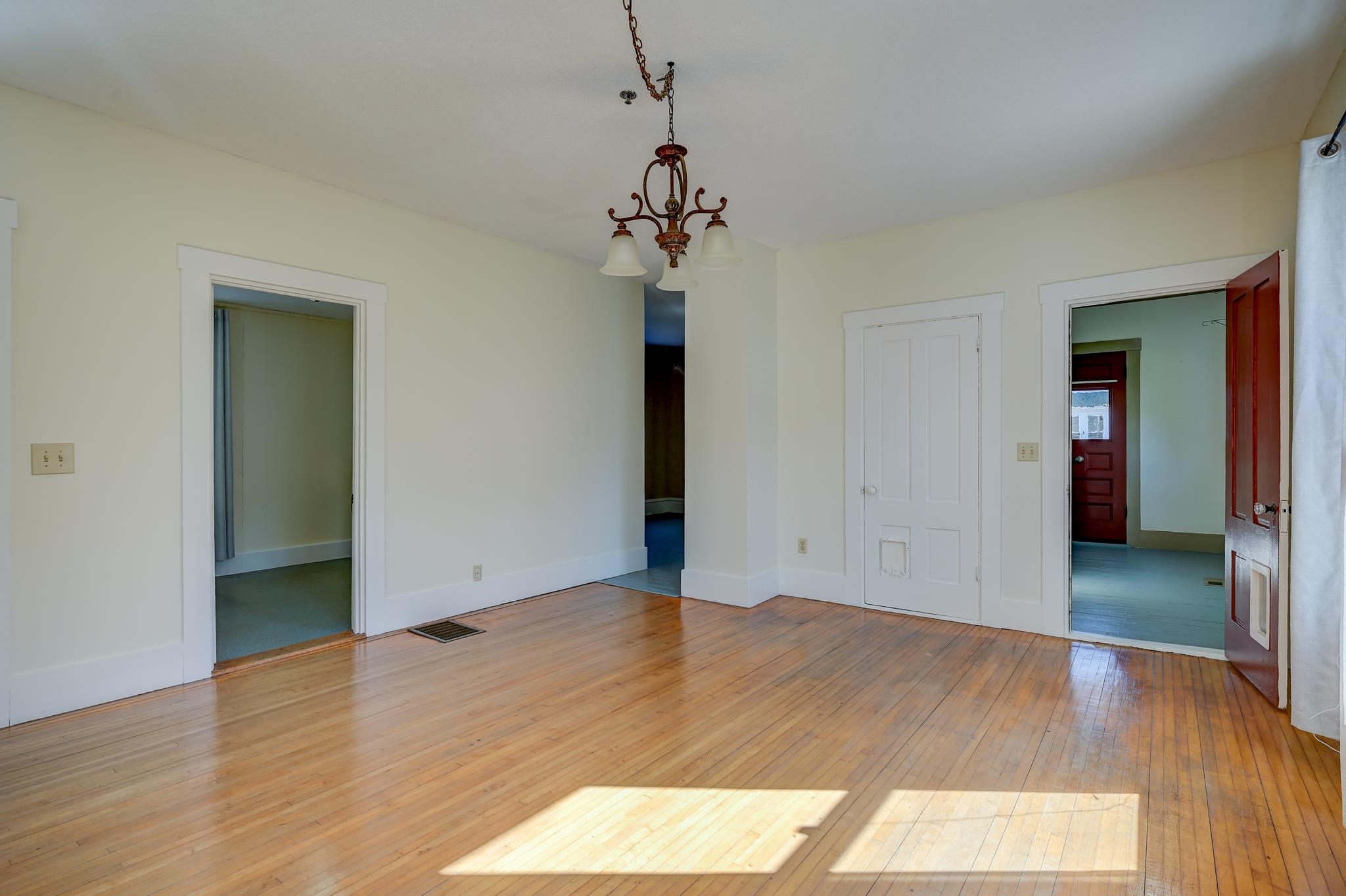 Empty room with polished hardwood floors, a chandelier, and doorways to adjoining rooms.
