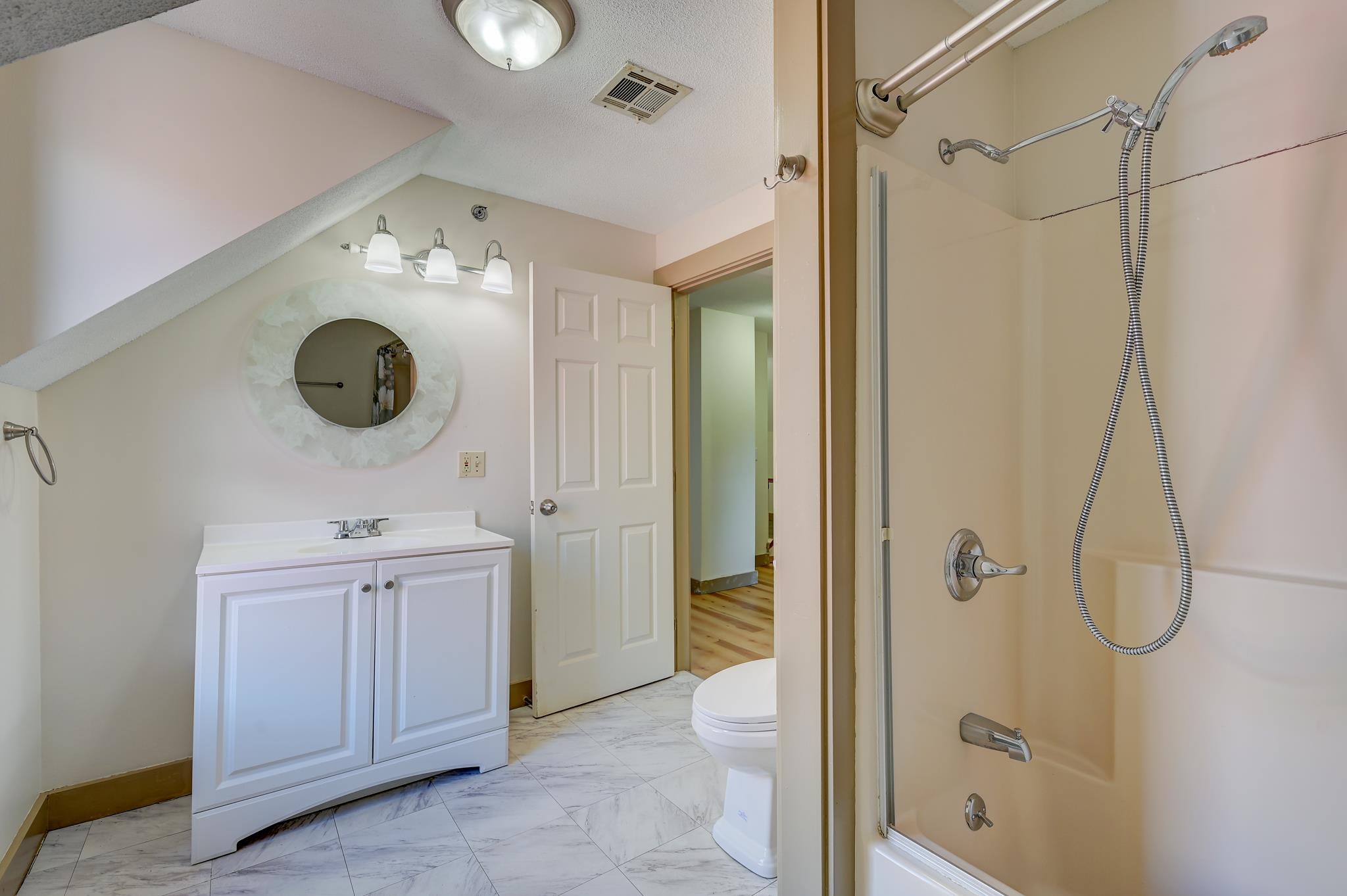 Bathroom with a white vanity, round mirror, marble-look floor, and shower with handheld fixtures.