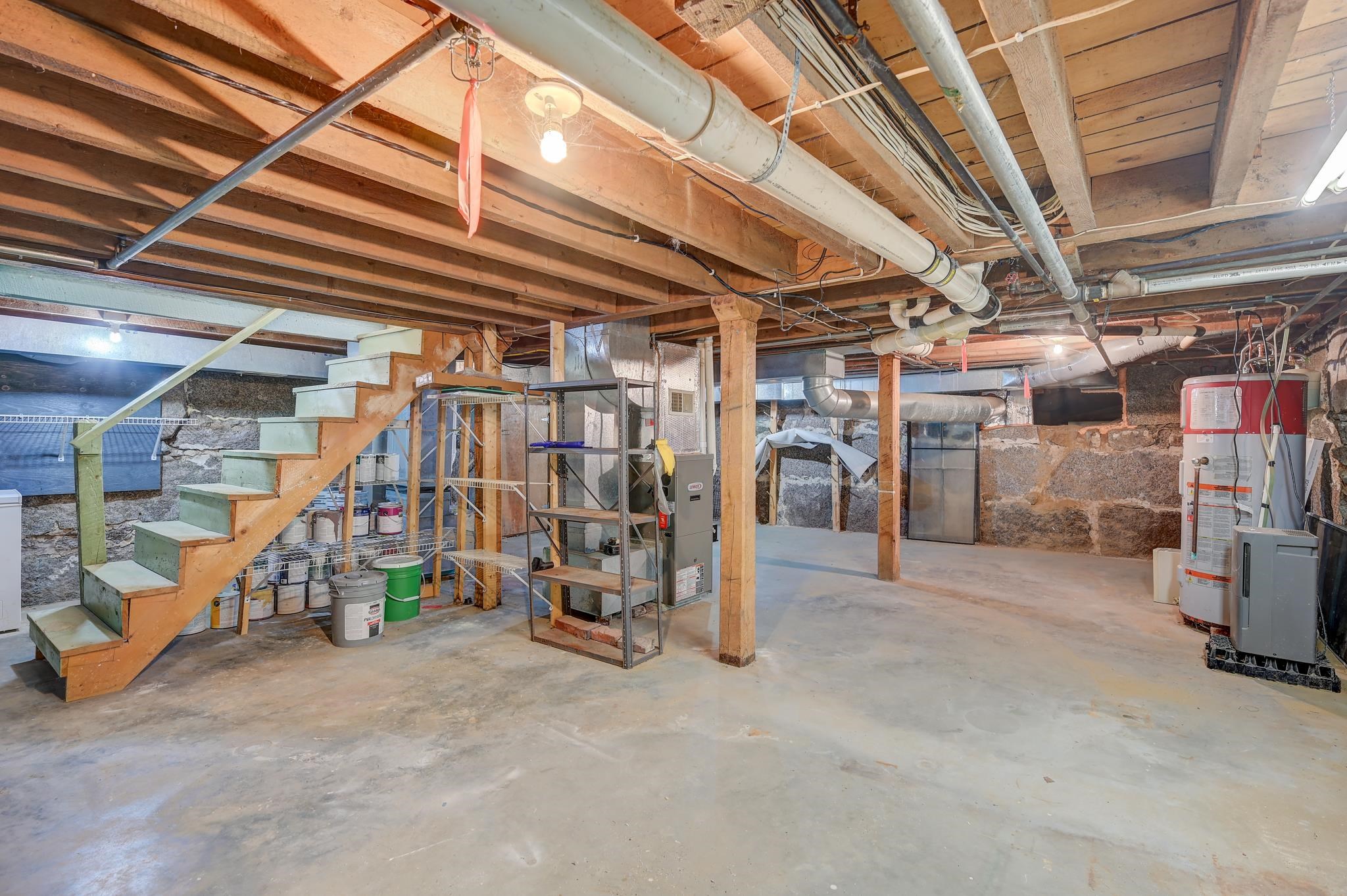 Unfinished basement with exposed beams, stone walls, wooden stairs, and mechanical equipment.