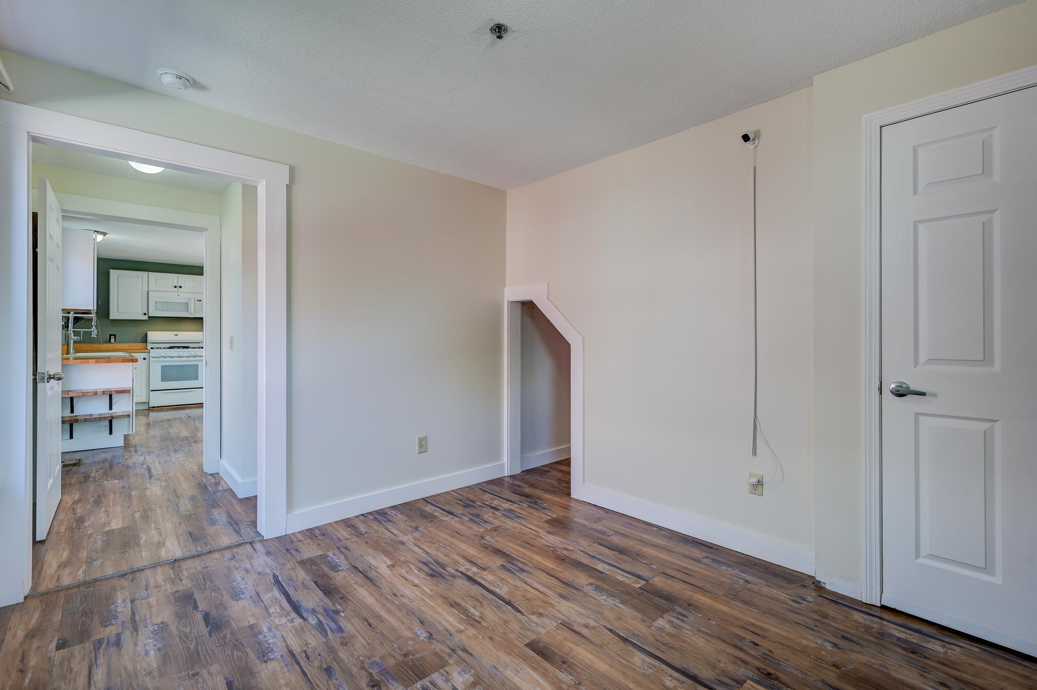 Unfurnished room with wood-look flooring, a kitchen doorway, and a small wall opening.