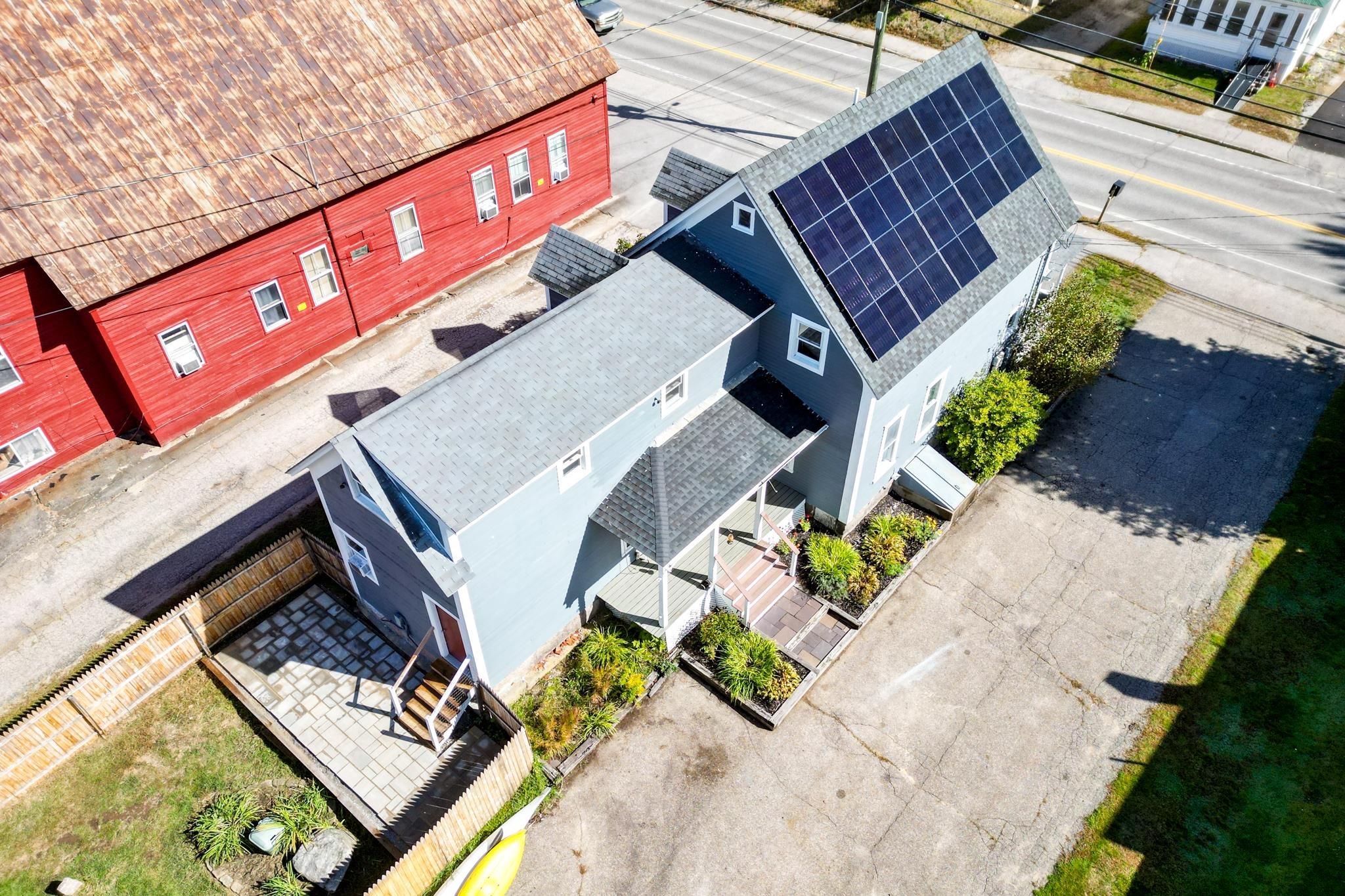 Aerial view of a blue-gray house with rooftop solar panels, a front porch, and landscaped beds.